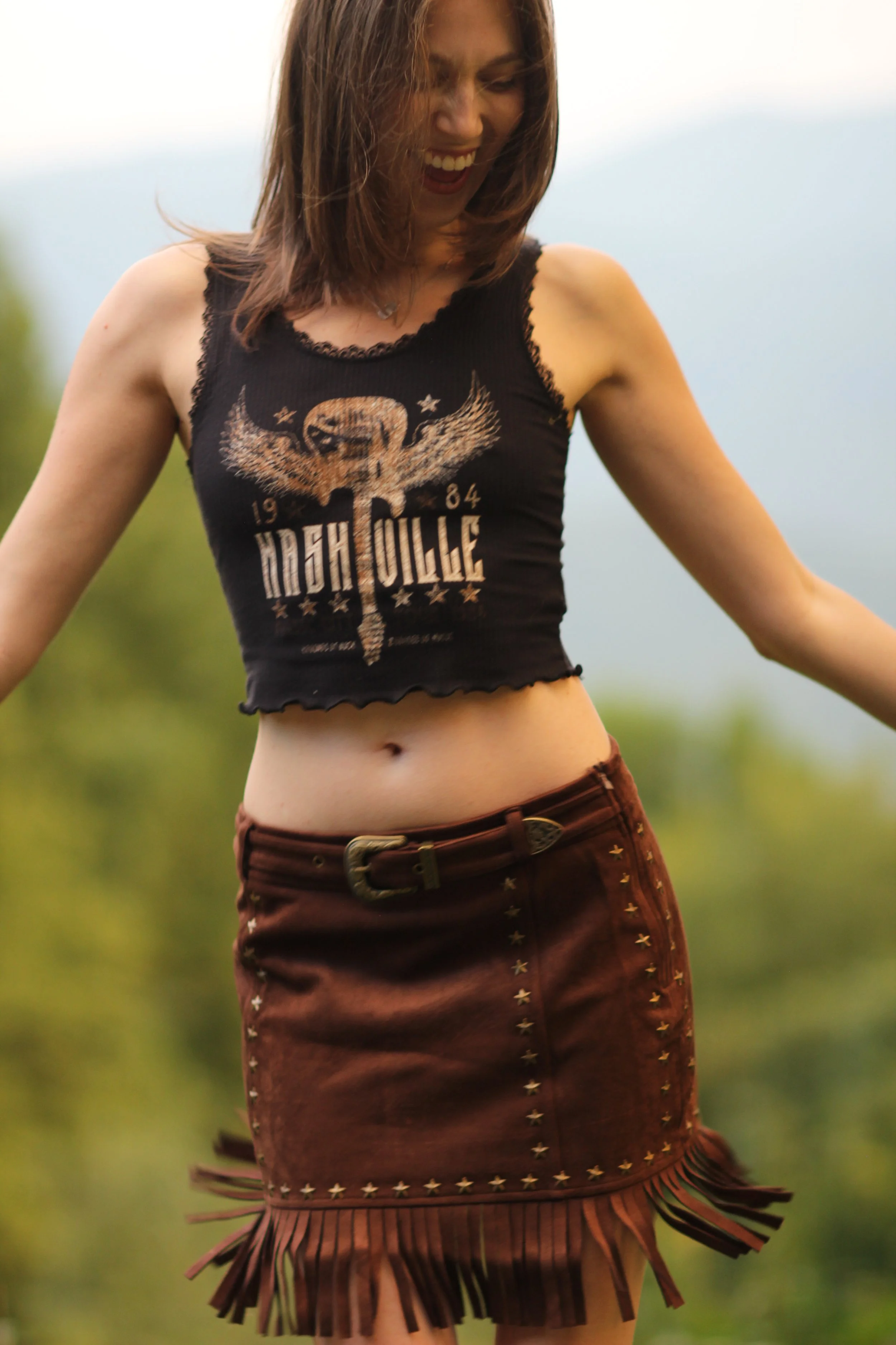 Woman wearing the Nashville Nights Fringe Skirt, a vegan suede mini skirt with studding and a statement buckle waist, front view