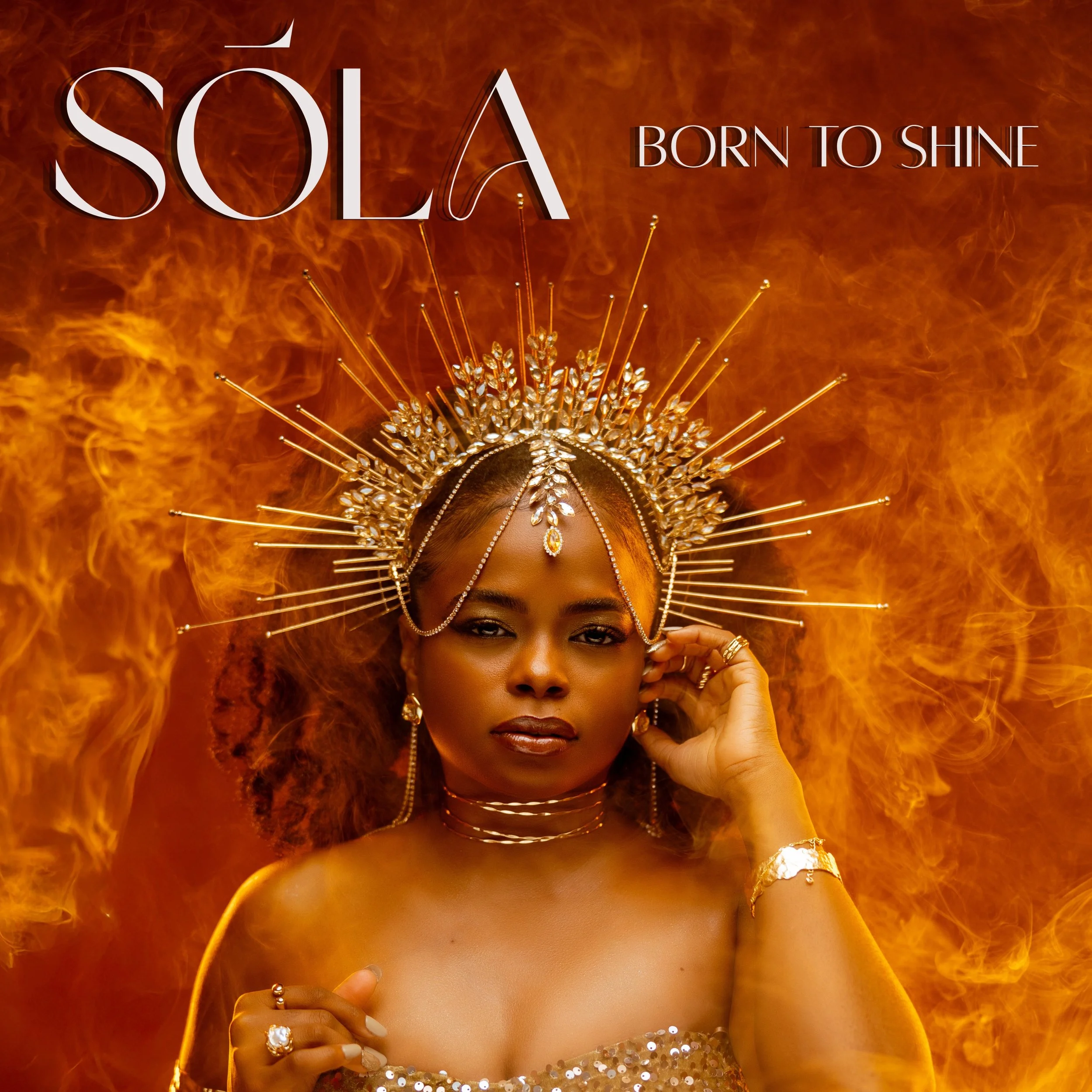 A woman wearing a decorative golden crown with spikes and rhinestones, surrounded by a fiery background with blazing flames, with the words "SÓLÀ BORN TO SHINE" in white and black lettering.