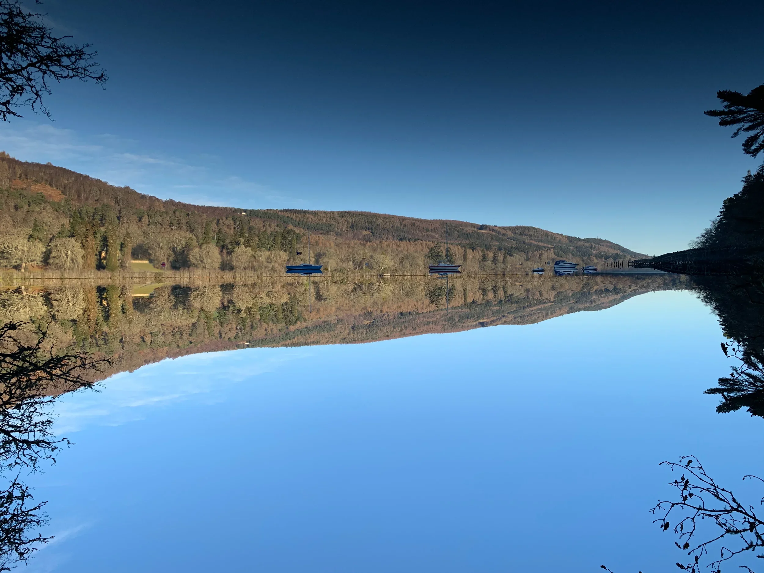 Boats moored at Loch Dochfour reflected in calm water