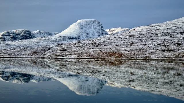 Snowy Highland Hill reflected in a still loch