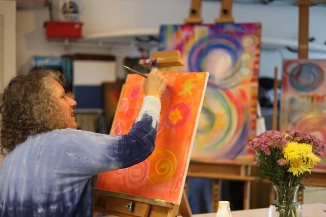 Denise Joy painting an orange and yellow canvas in an art studio.