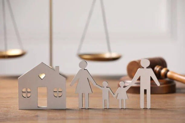 Paper cutout figures of a family holding hands, a house, and a scale in the background, symbolizing family, home, and legal matters.