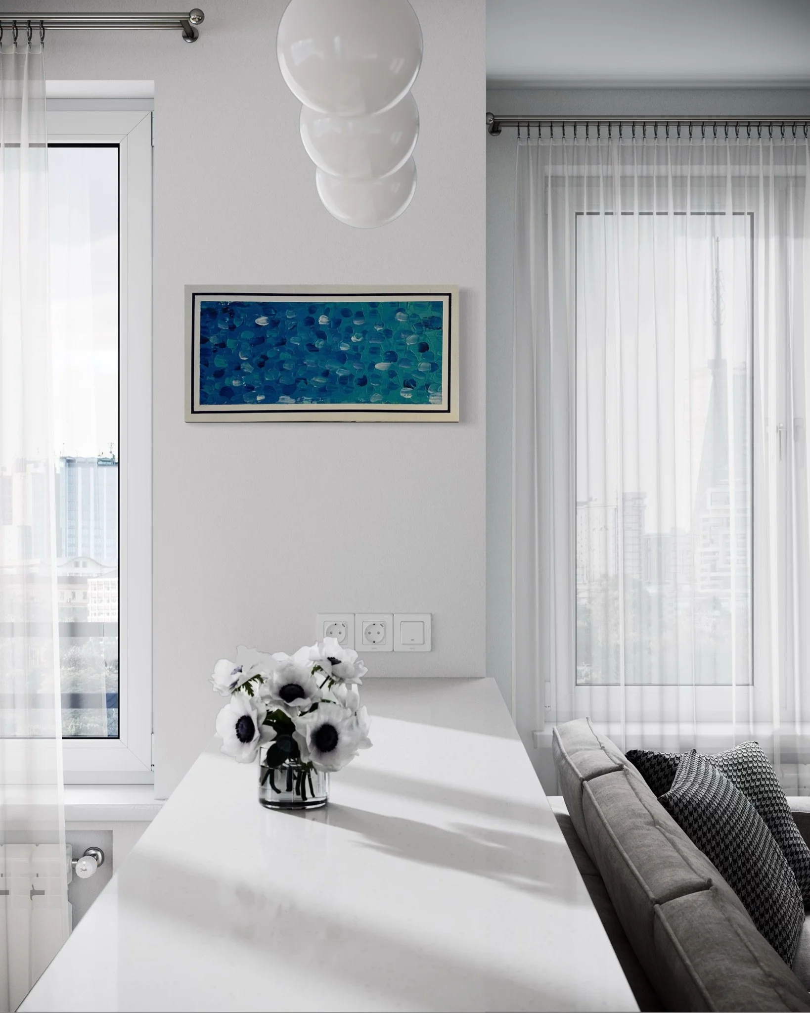 A modern living room with large windows and sheer curtains, a white table with a vase of black-and-white flowers, a couch with patterned pillows, a framed blue abstract art piece on the wall, and a ceiling light fixture.
