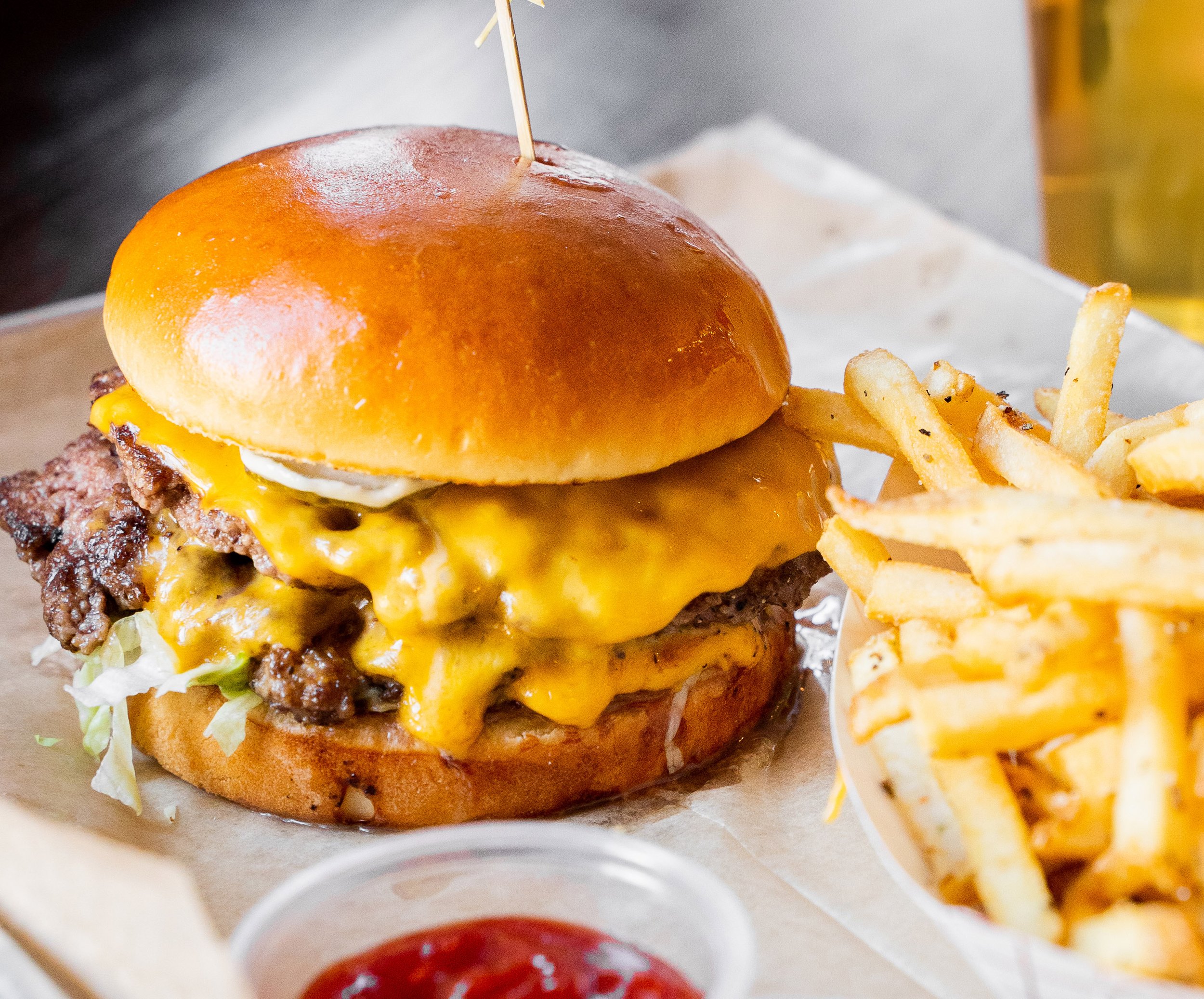 A close-up of a cheeseburger with a shiny bun, melted cheese, and a beef patty, with a side of French fries.