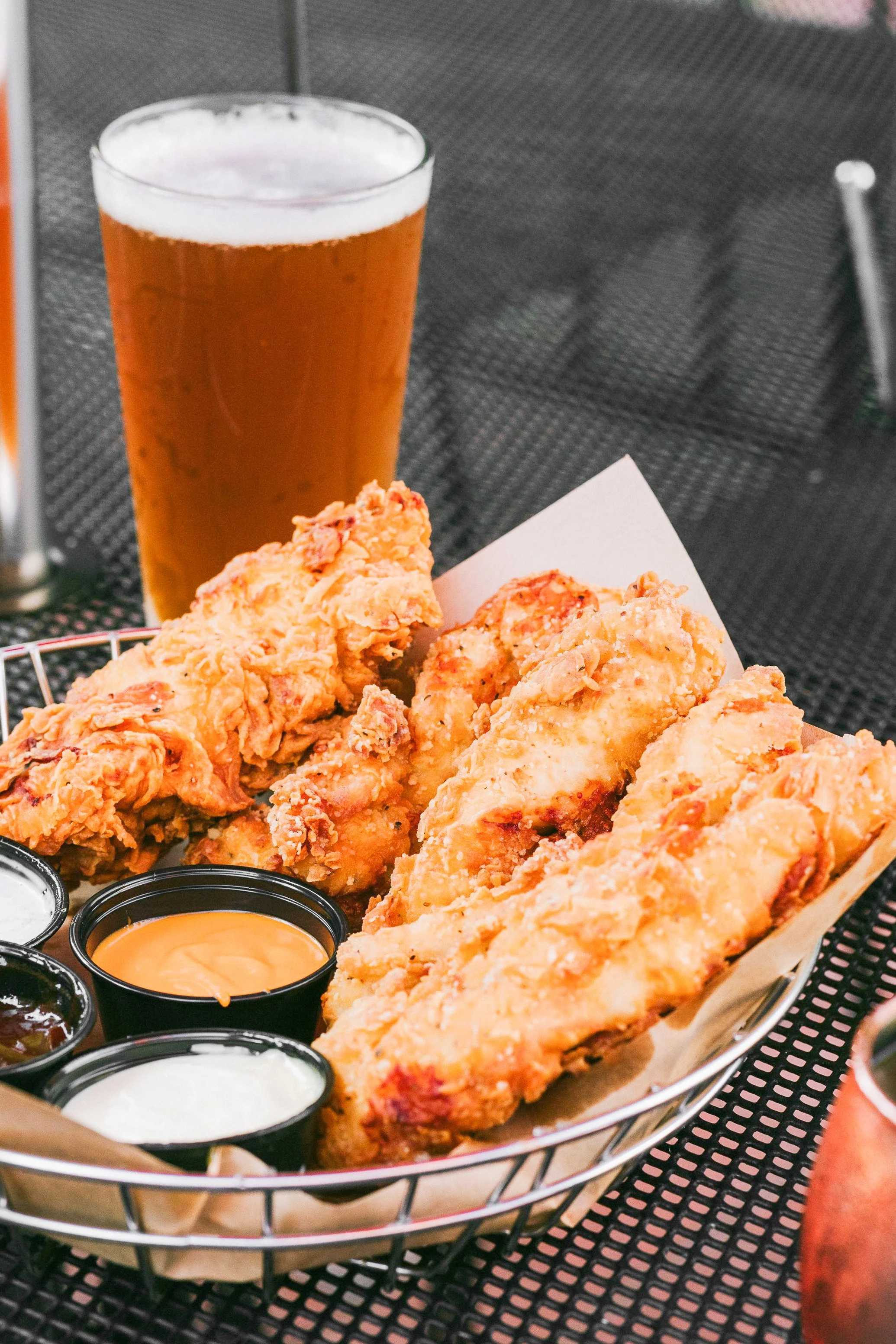 Basket of fried chicken with three dipping sauces and a glass of beer in the background.