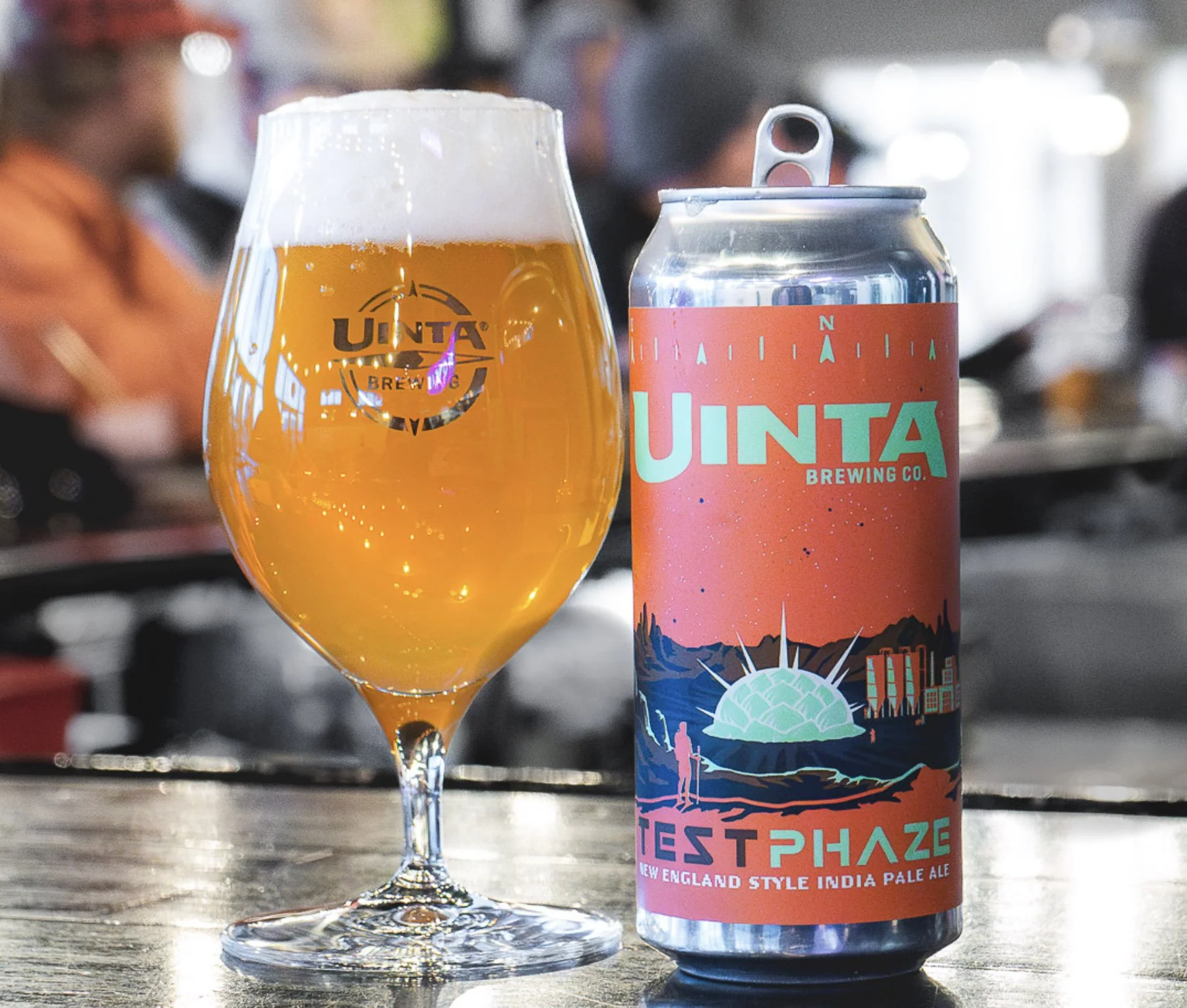 A glass of golden beer with a foamy head and a can of Uinta brewery beer featuring a colorful mountain landscape mural.