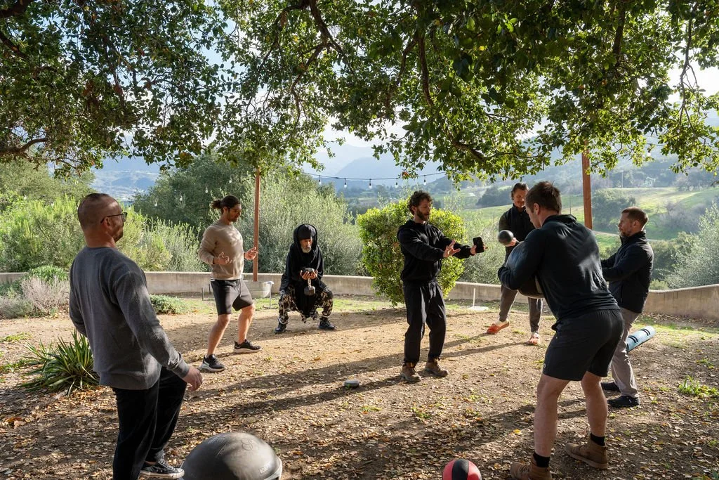 Group of people doing fitness exercises outdoors under a tree with scenic hills in the background.