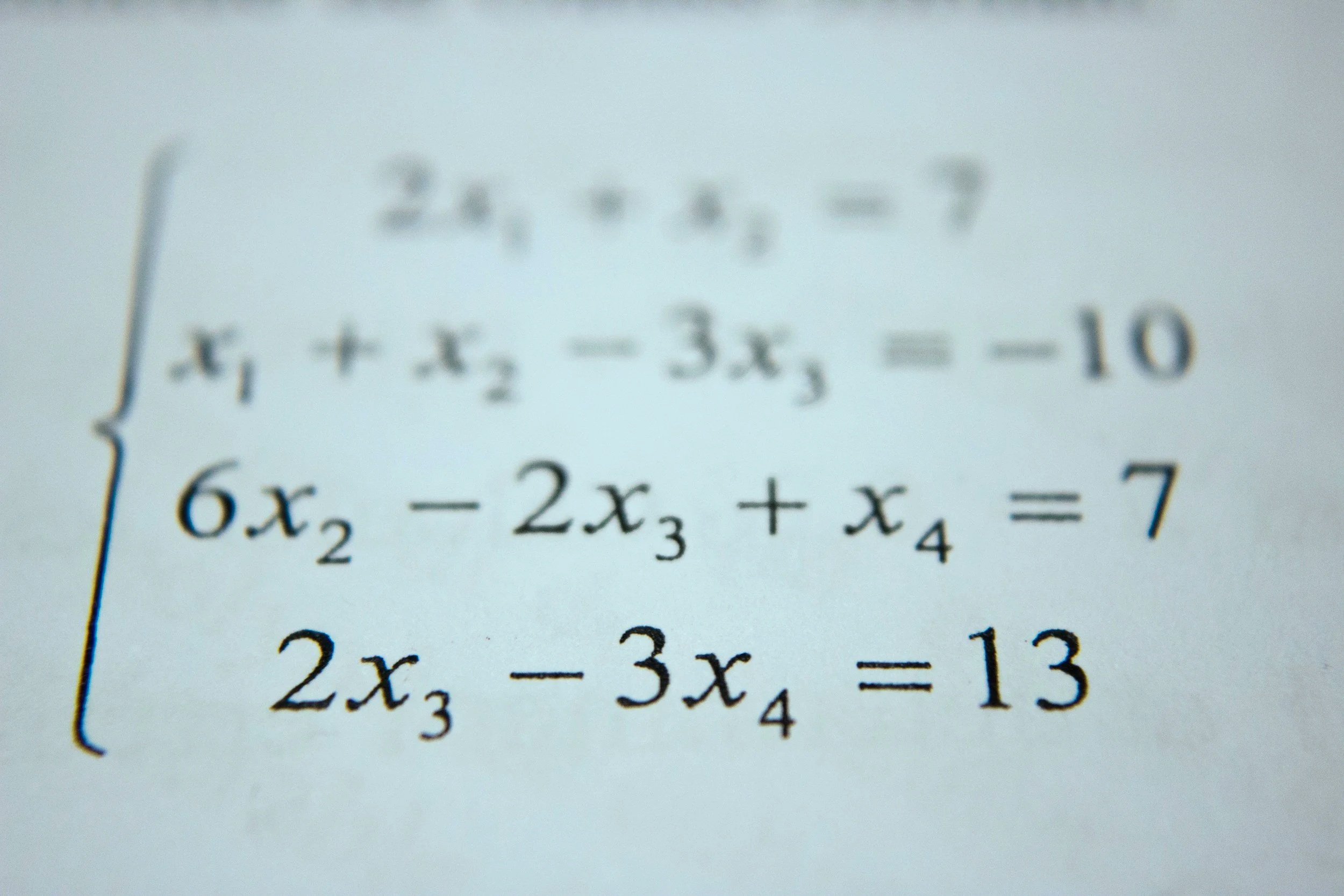 Close-up of a math problem on a printed sheet, showing equations with variables and coefficients, with some blurred text.