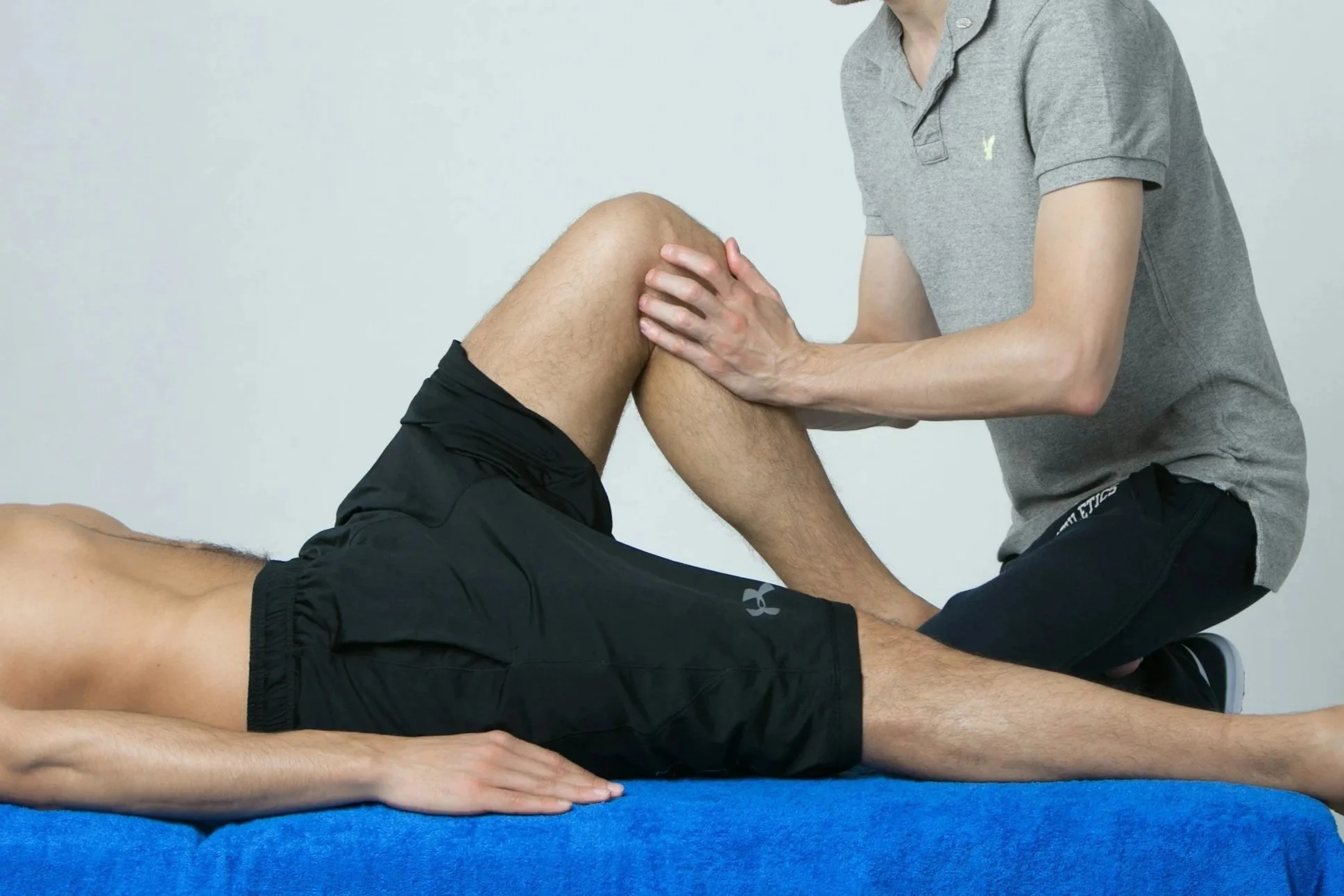 A person lying on their back on a blue mat receiving physical therapy or chiropractic treatment from a healthcare professional.