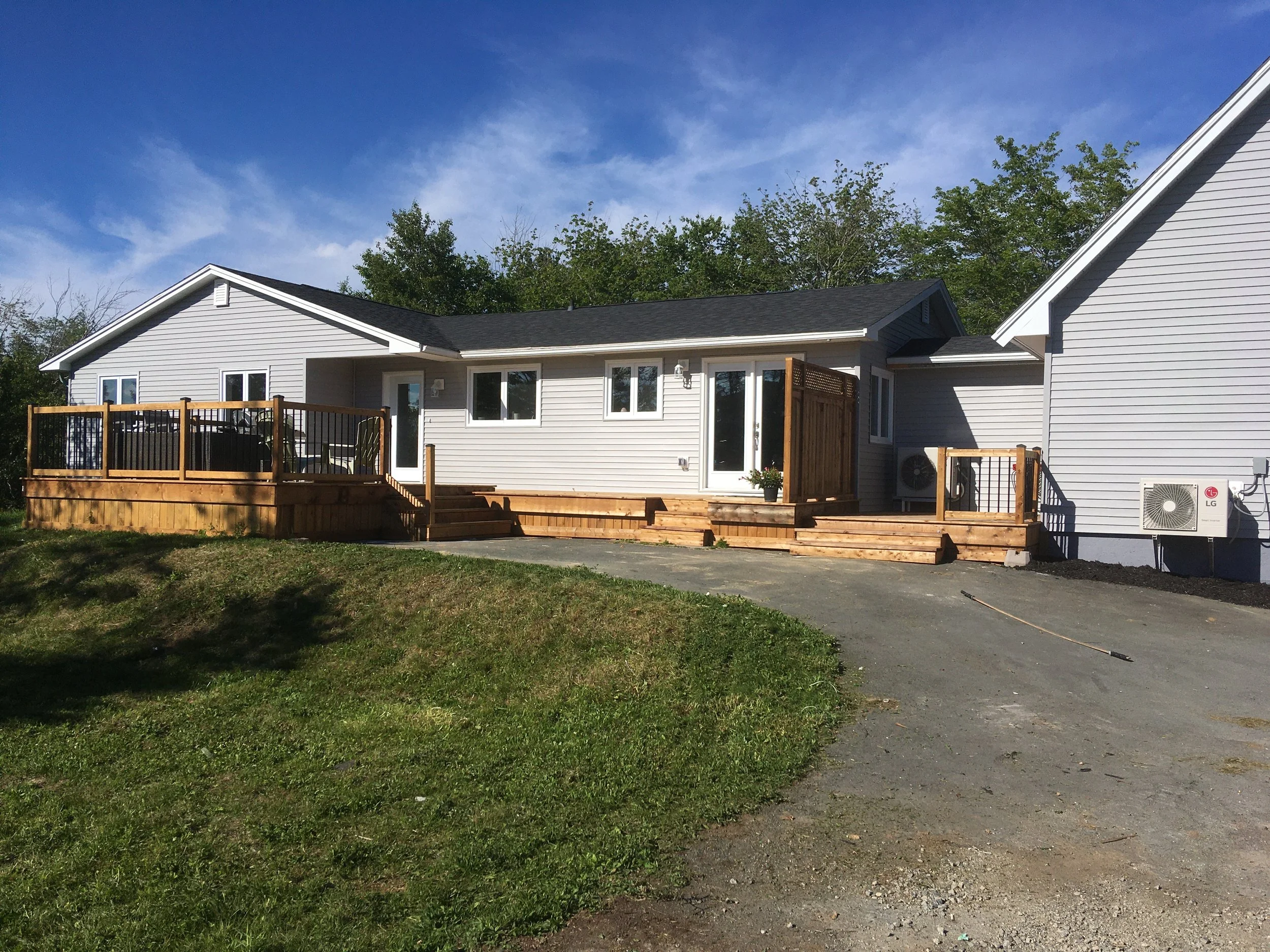 A suburban house with gray siding, a wooden deck, and a backyard, under a blue sky with some clouds.