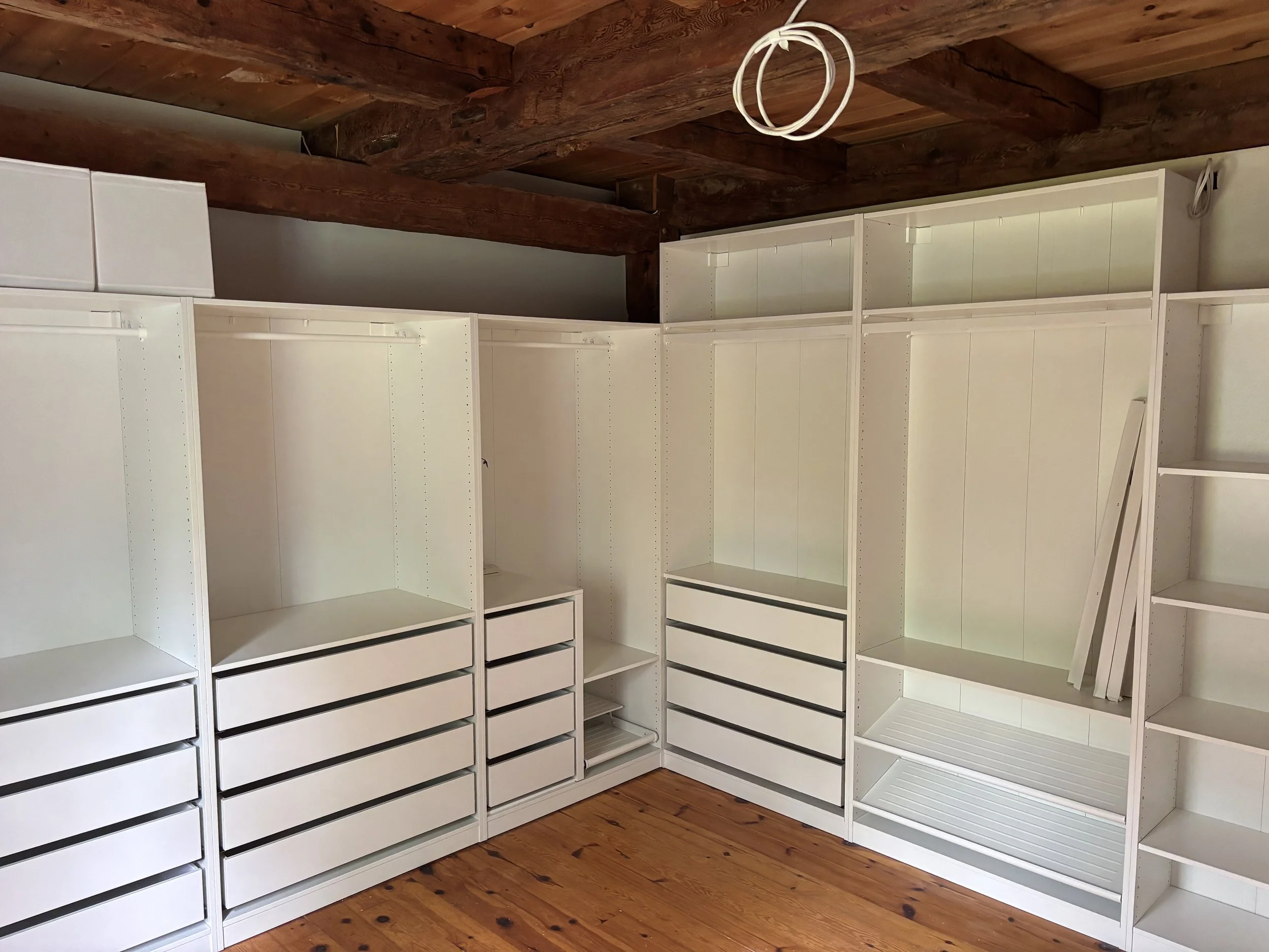 Empty white shelving units in a room with wooden flooring and exposed wooden ceiling beams.