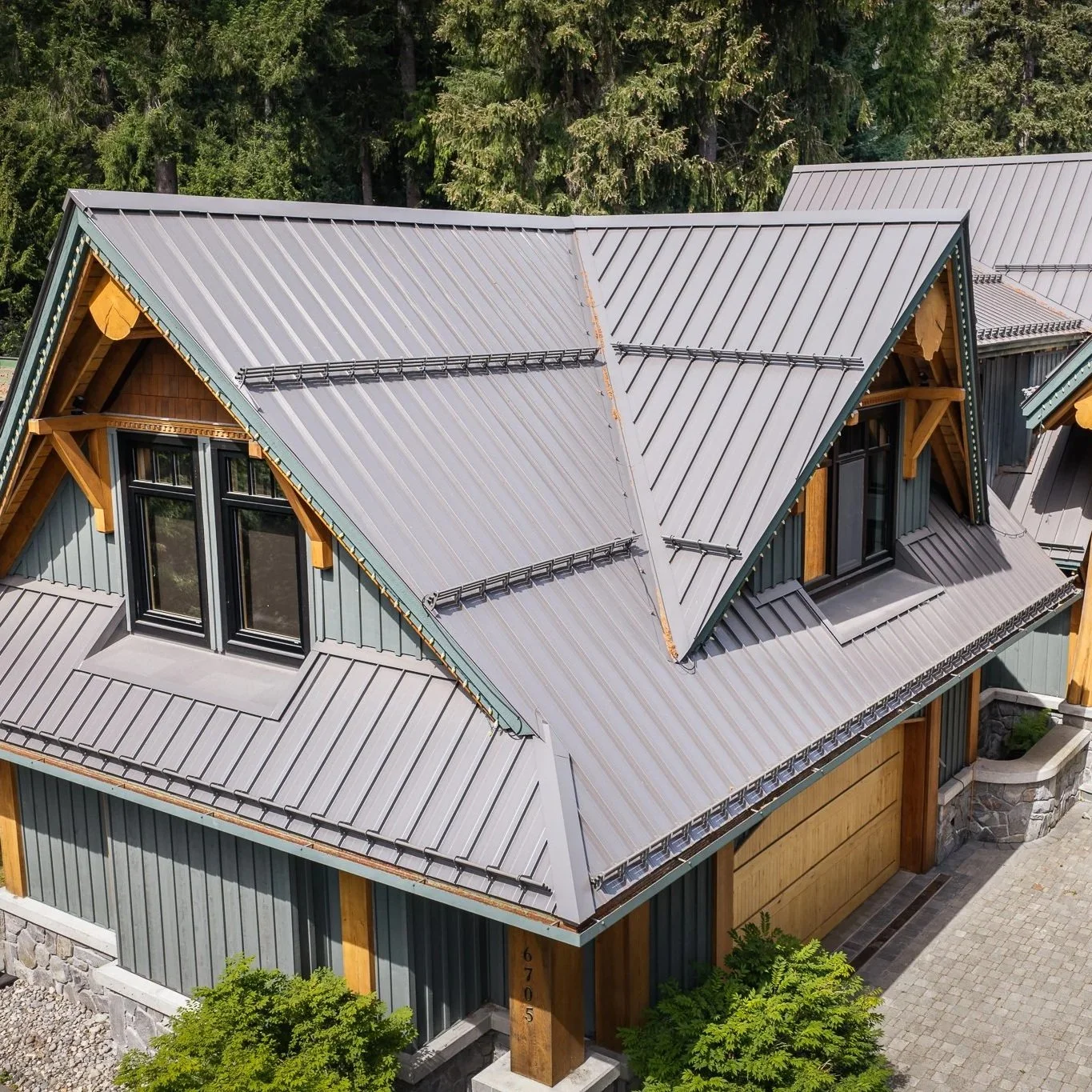 Close-up of a mountain home with a standing seam metal roof, dormers, and custom flashing, surrounded by mature trees.
