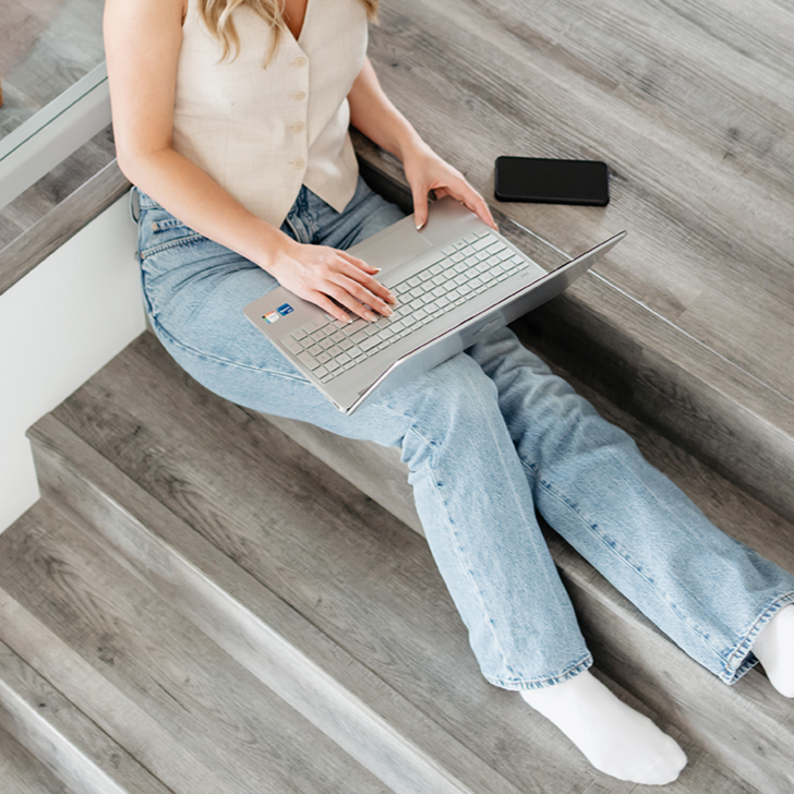 Person sitting on stairs using a laptop, with a phone nearby.
