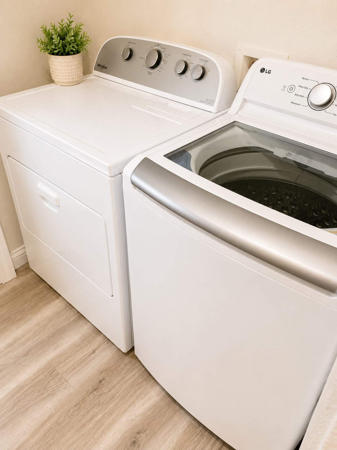 A laundry room with a white top-loading washing machine and a white dryer. A potted green plant is placed on top of the dryer.