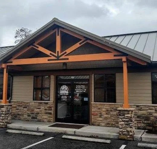Front entrance of a commercial building with a stone and siding exterior, wooden beams framing the entrance, and a glass door with signs on it.
