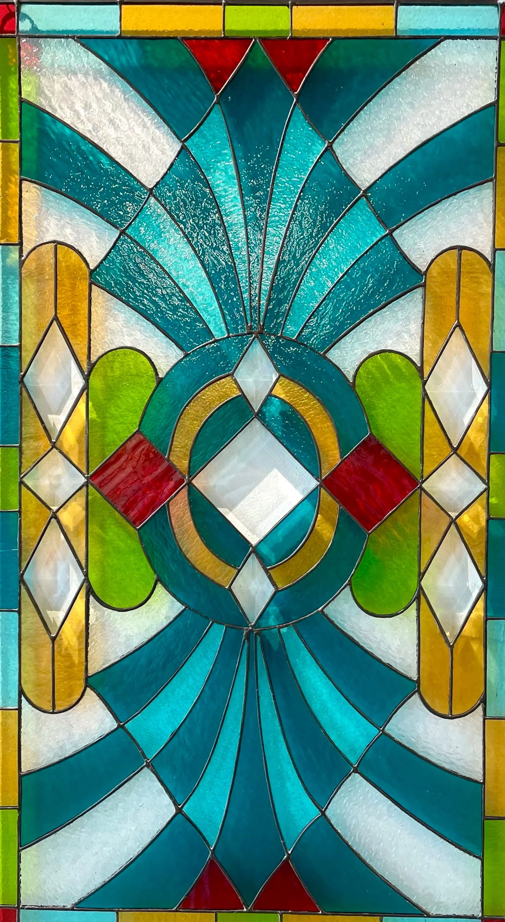 Colorful stained glass window with geometric and floral design, featuring shades of blue, white, red, green, and yellow.