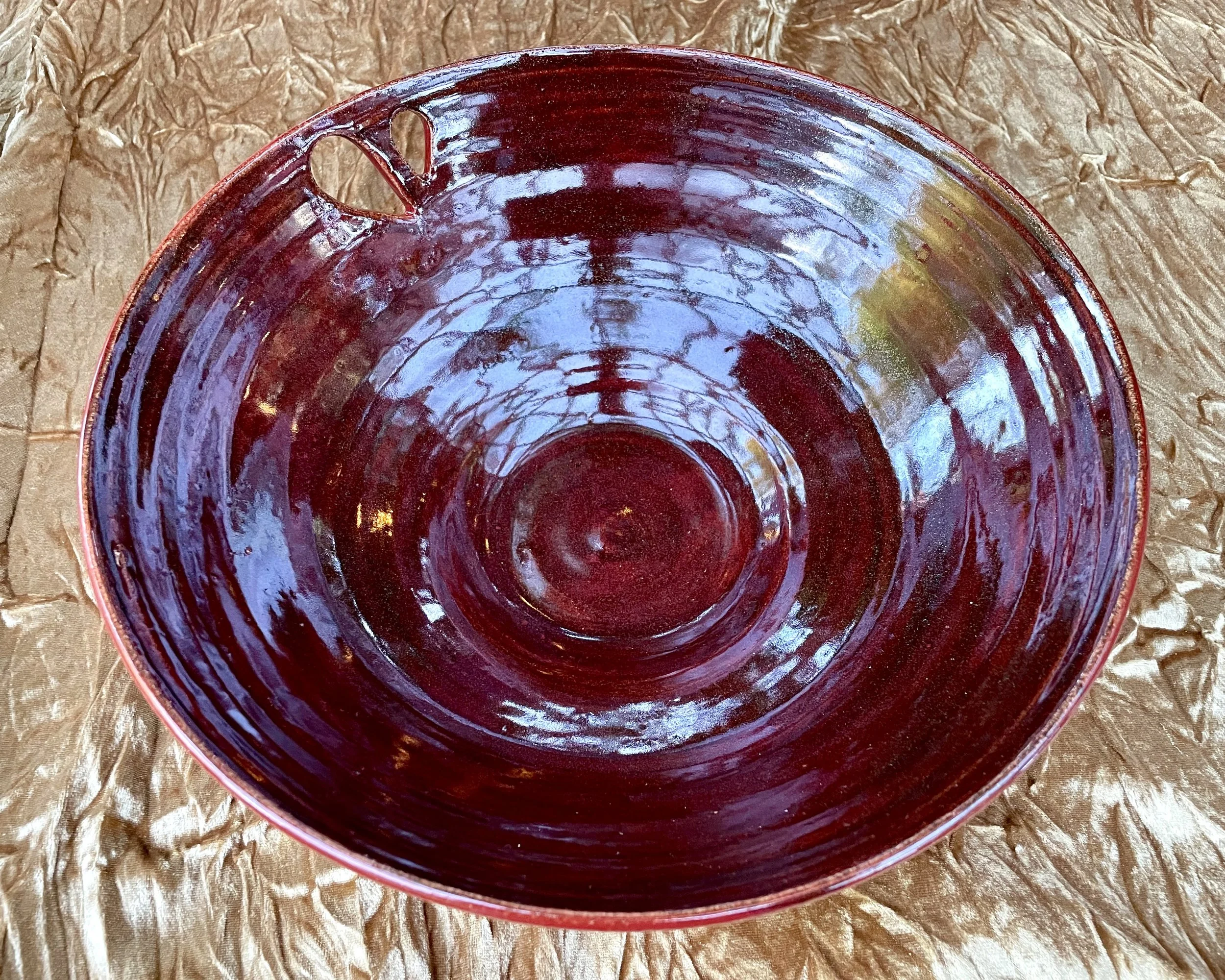 A close-up view of a deep red ceramic bowl with a glossy finish, placed on crumpled brown parchment paper.
