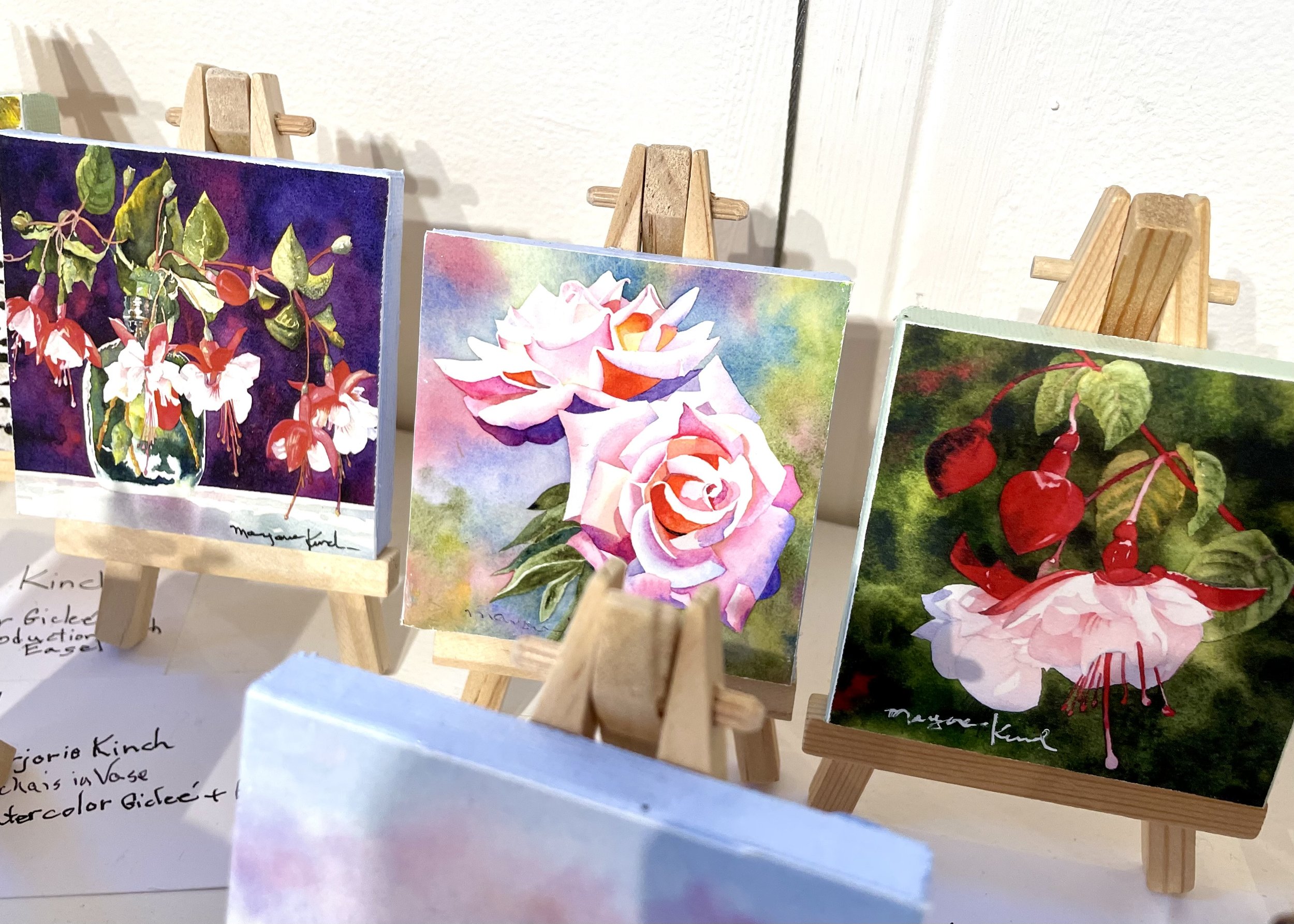 Small watercolor paintings of flowers displayed on miniature wooden easels.