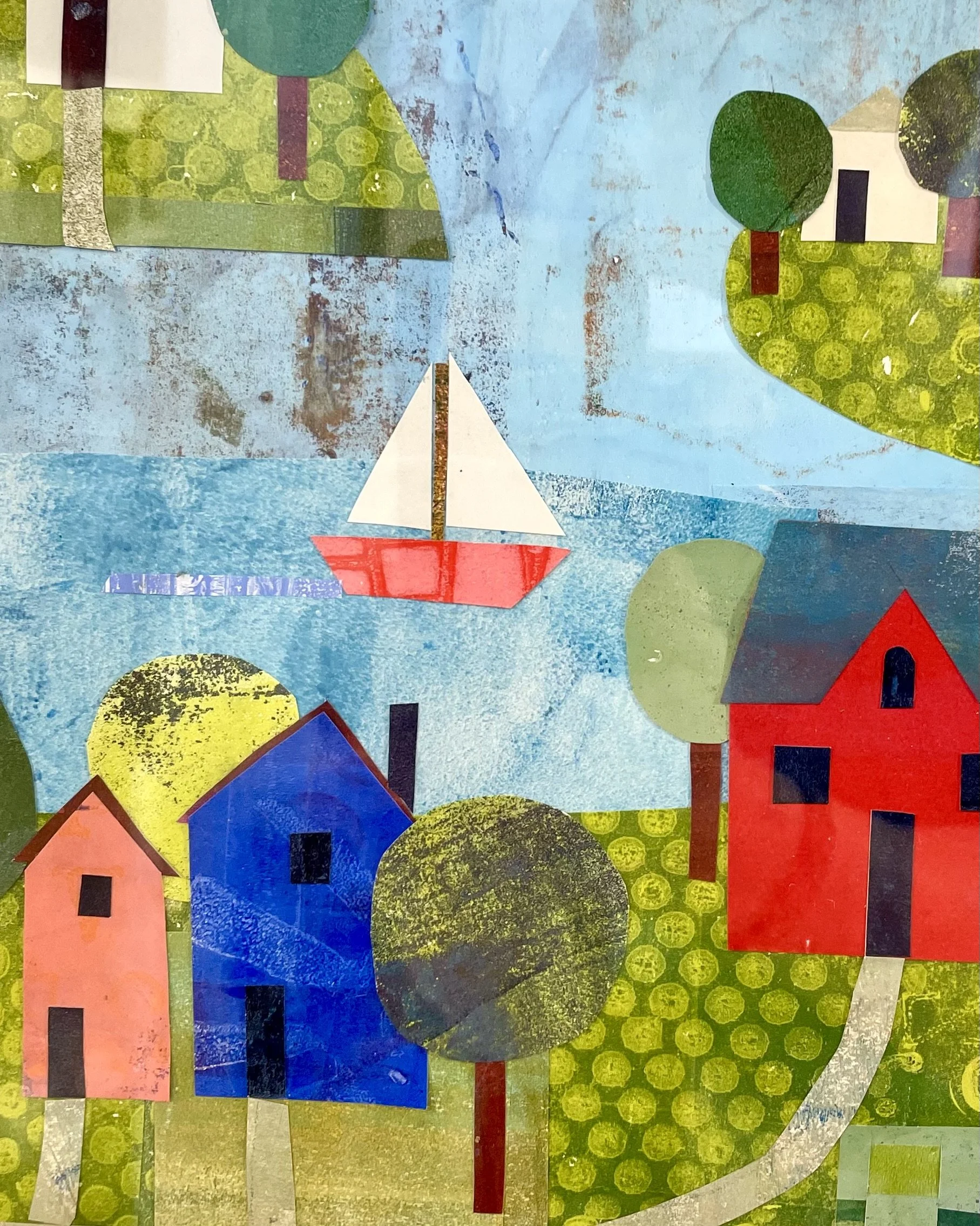 A collage made of cut paper pieces depicting a sailboat with a red hull and white sail on blue water, surrounded by green trees, colorful houses, and a background of textured blue sky.