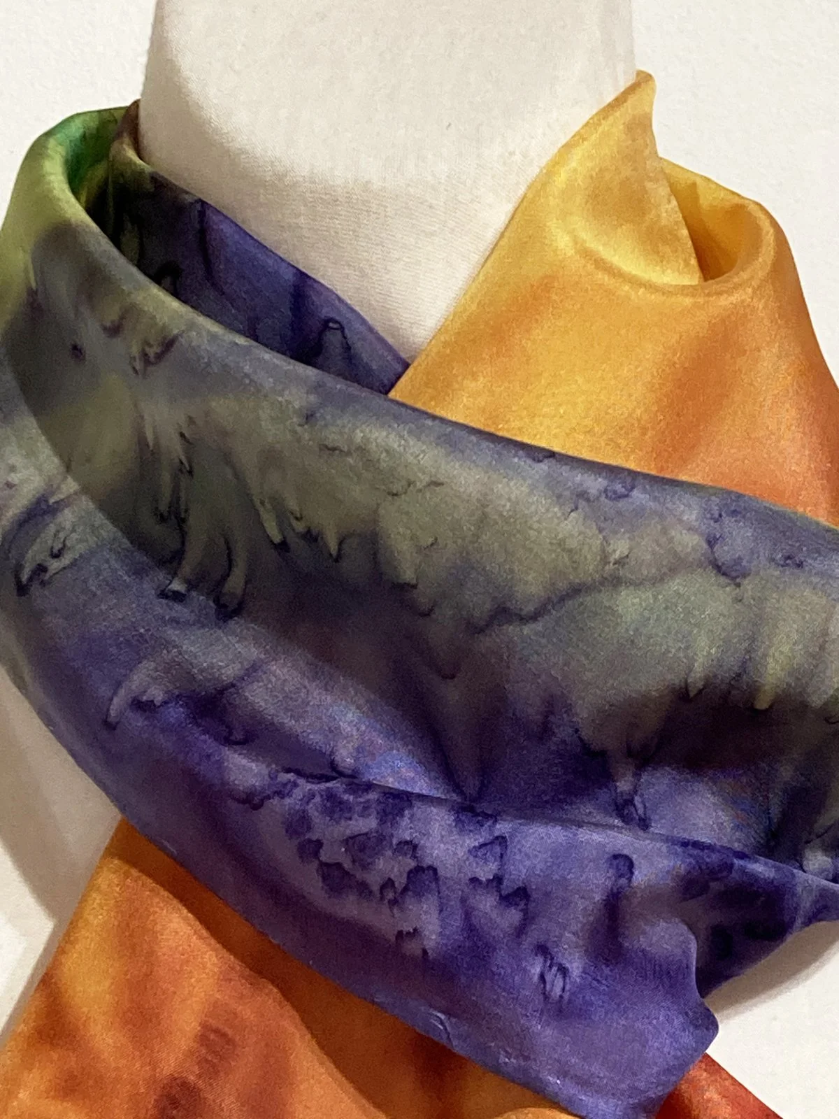 A multicolored silk or satin scarf with a floral pattern, featuring shades of purple, green, and orange, draped over a white mannequin.