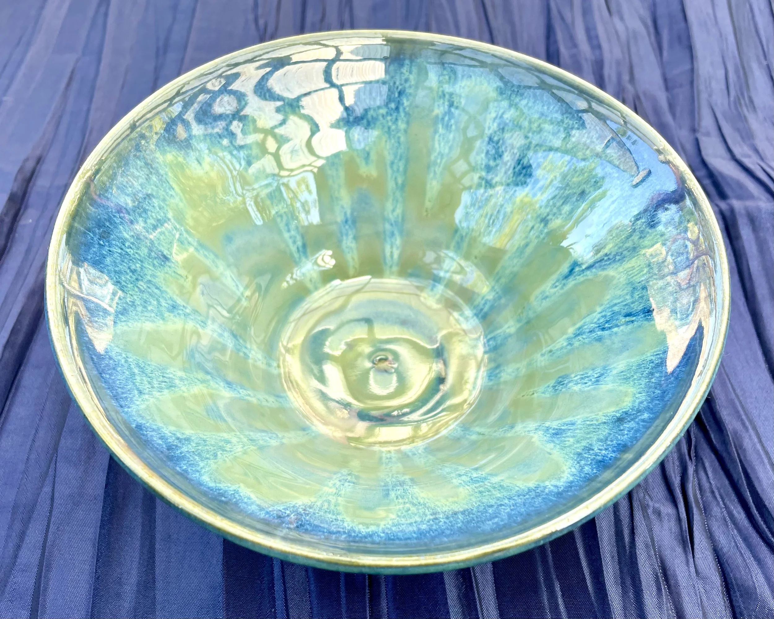 Close-up of a glass bowl with colorful iridescent patterns, sitting on a blue wooden surface.