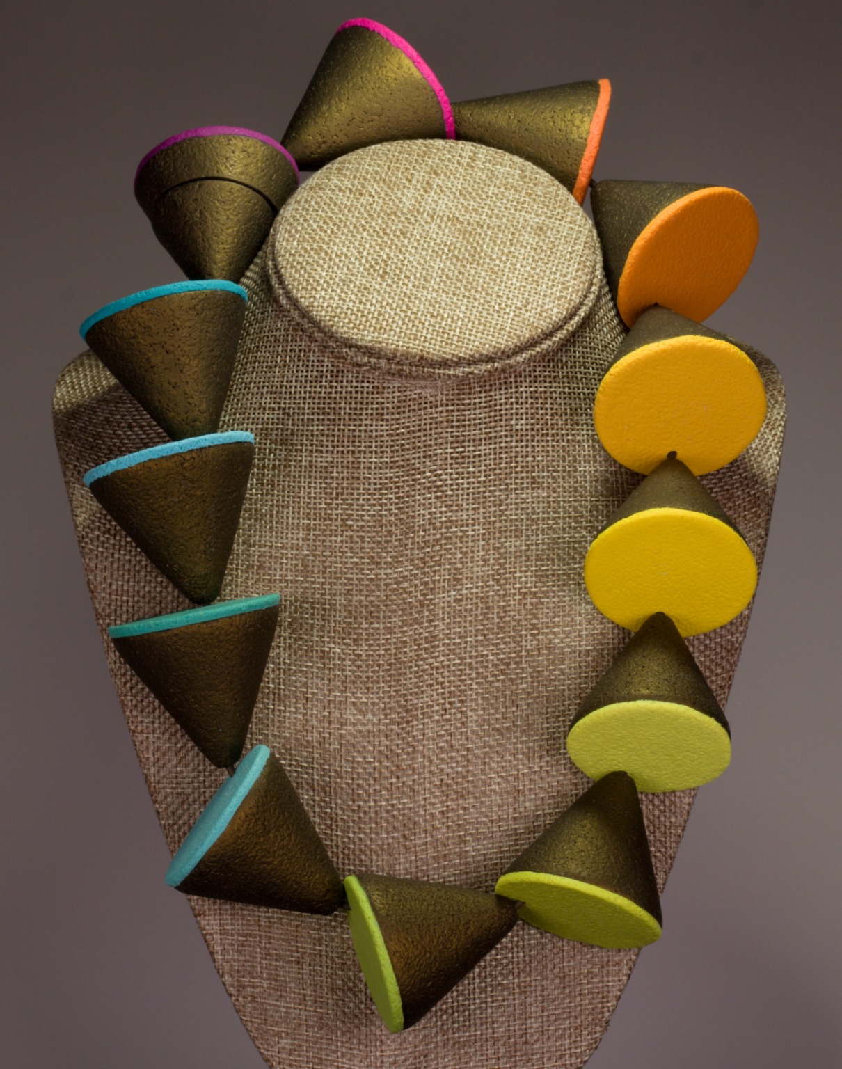 Colorful geometric sculpture with cone and semi-circle shapes on a textured fabric backdrop.