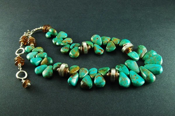 A turquoise beaded necklace with metal accents and a silver clasp, spread on a black background.