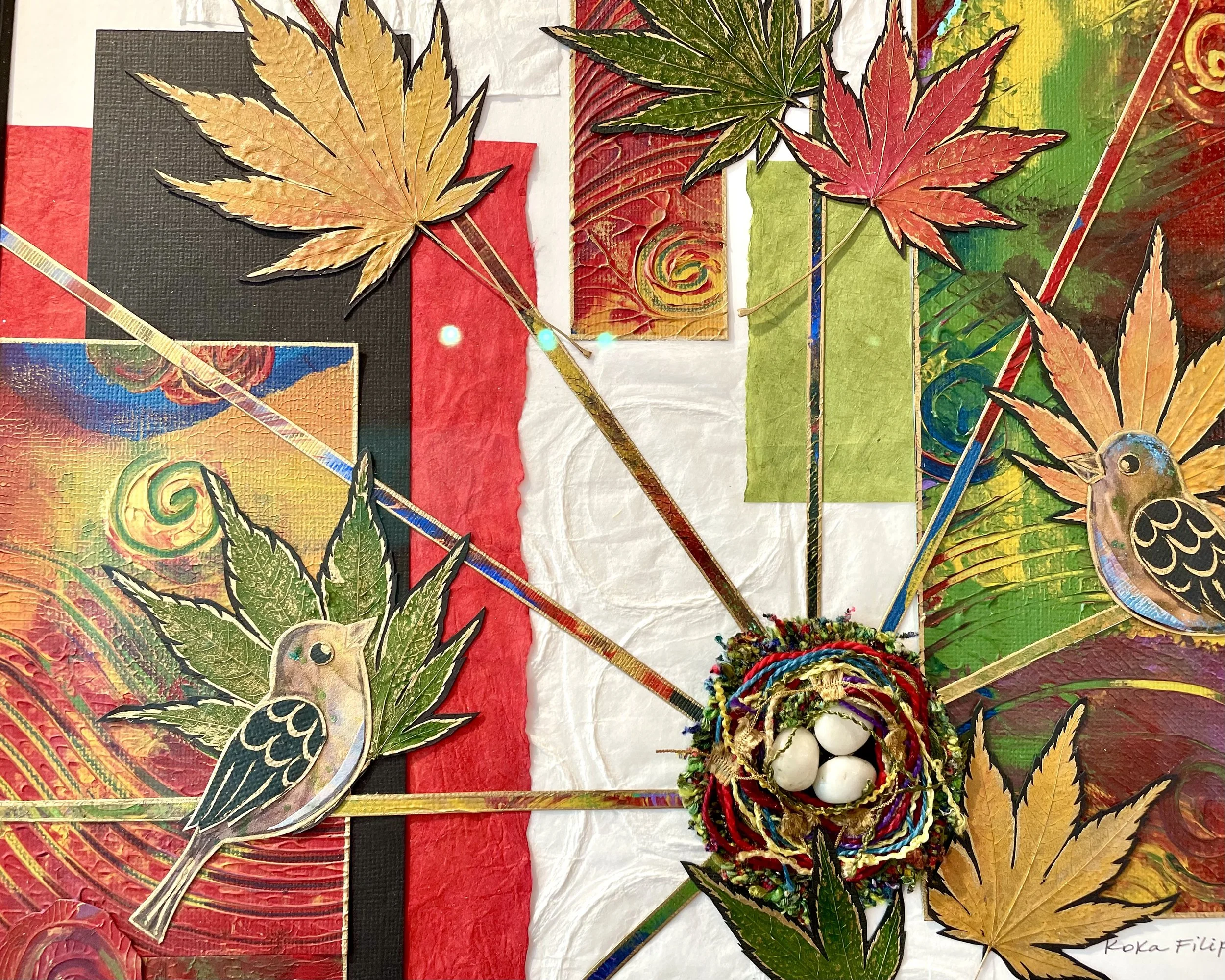 Colorful art display with dried autumn leaves, painted paper, and decorative birds, arranged on various colored backgrounds.