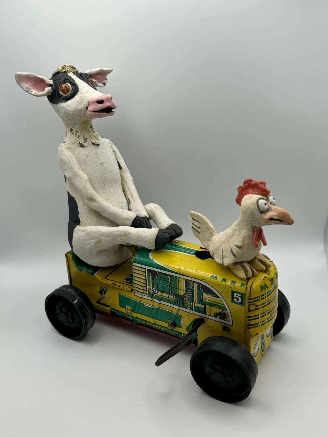 Sculpture of a cow and a chicken riding a yellow toy vehicle
