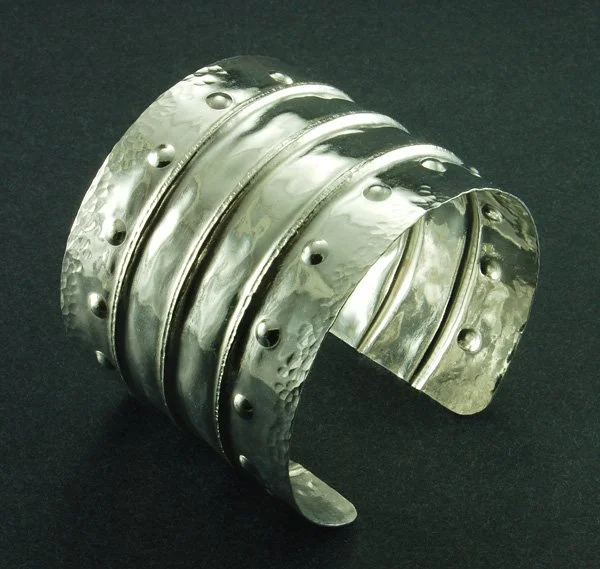 Silver metal cuff bracelet with a hammered texture and dotted accents.