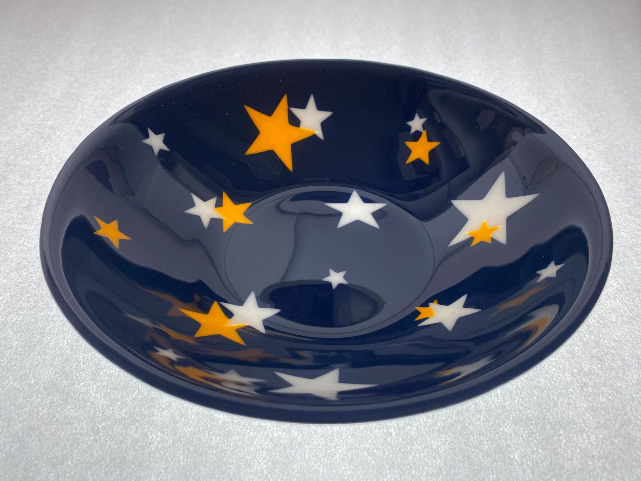 A ceramic bowl with a dark blue interior decorated with white and yellow stars on a white textured surface.