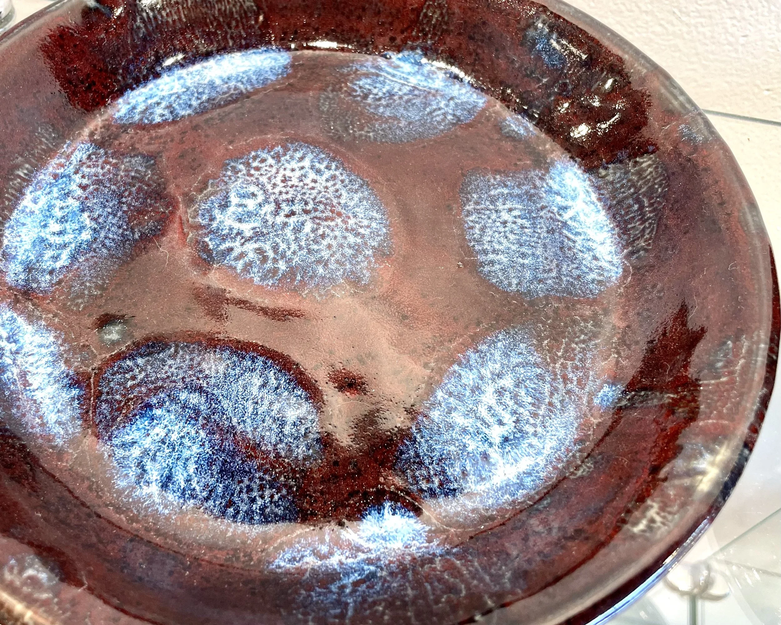 Close-up of a red glass dish with a textured surface, showing blue and white glasses or reflections on the inside.