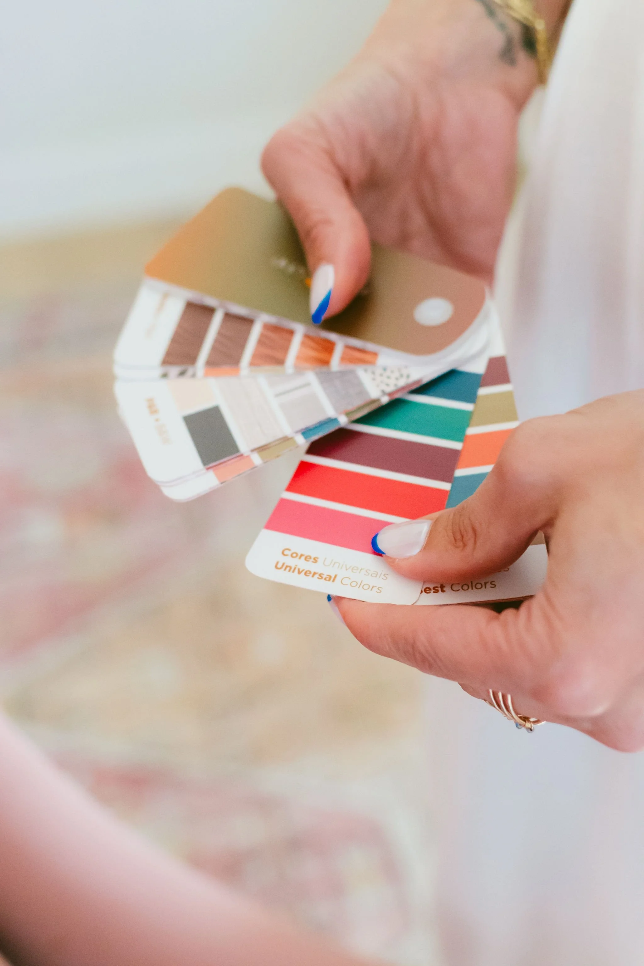 Close-up of a person's hand holding a paint color swatch fan, with various paint color samples visible.