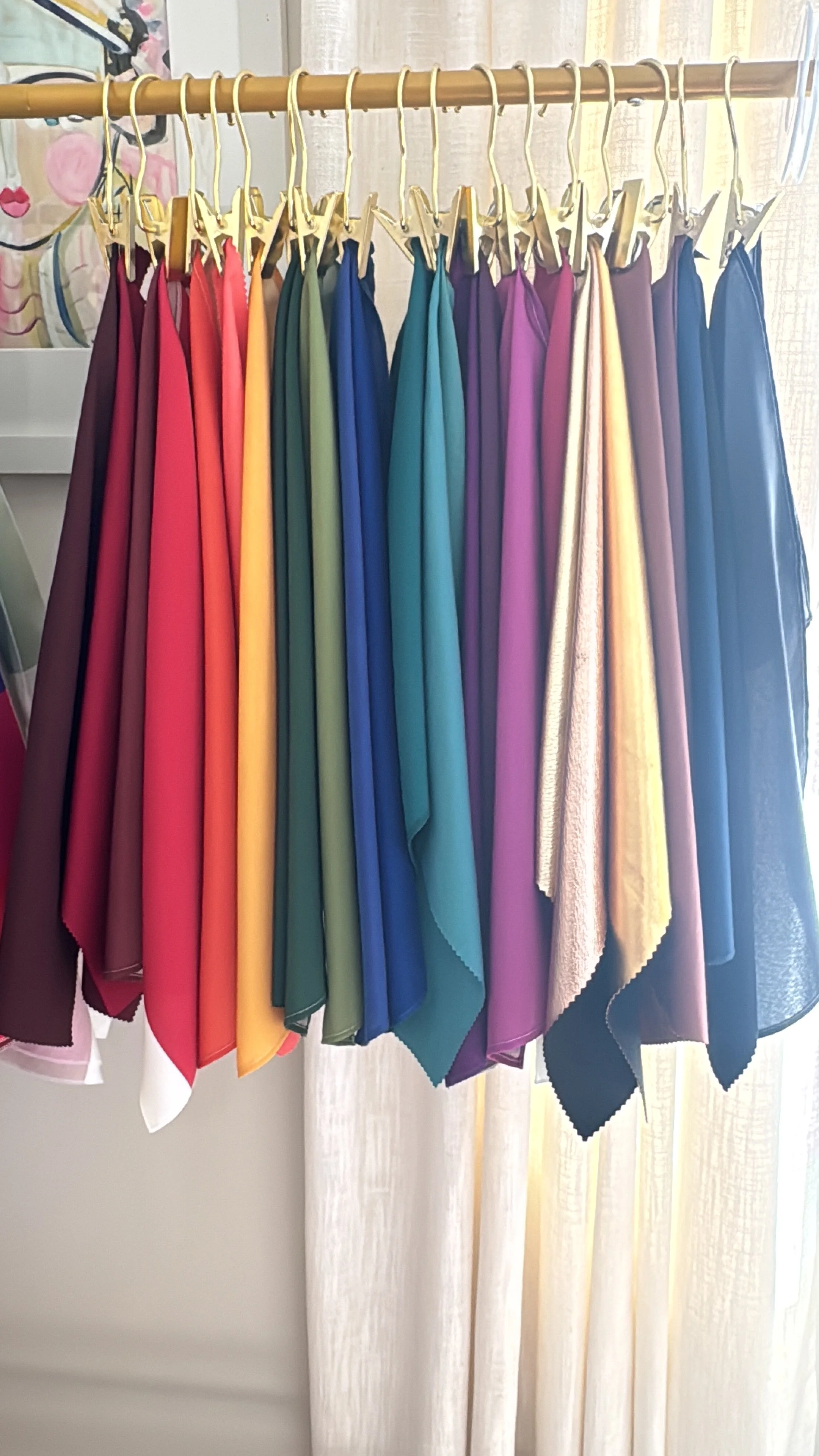 A collection of colorful fabric swatches hanging on wooden hangers on a horizontal rod.