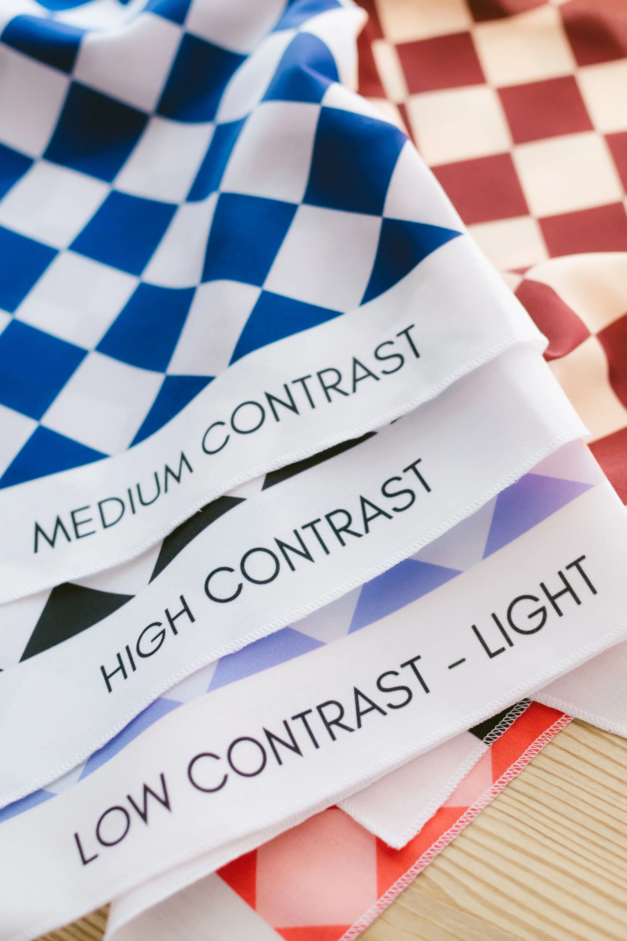 Close-up of multiple checkered kitchen towels with different color patterns, labeled with their light contrast levels from high contrast to low contrast.