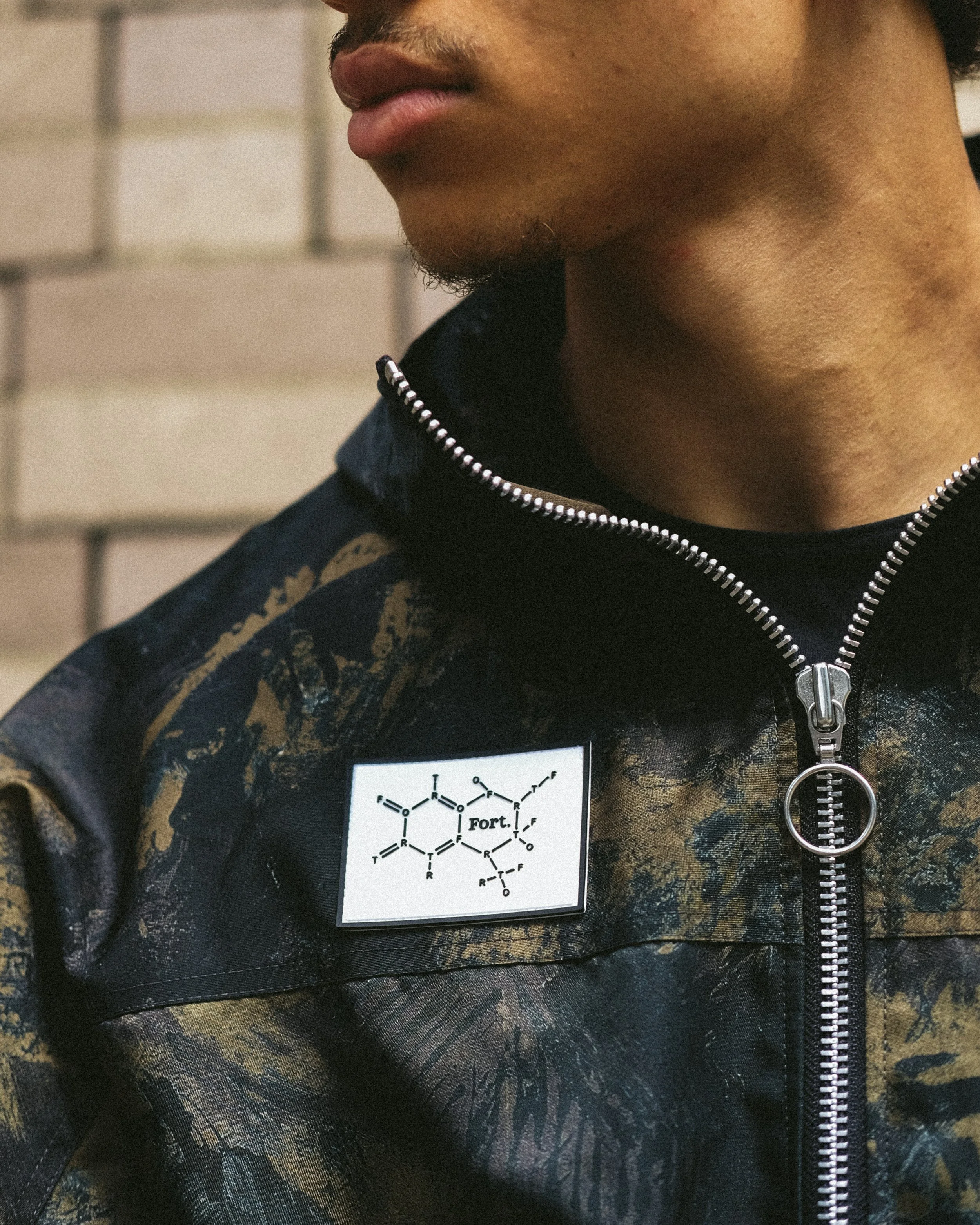 Close-up of a person wearing a black jacket with a zipper, and a white patch featuring a chemical diagram labeled 'Fort.'