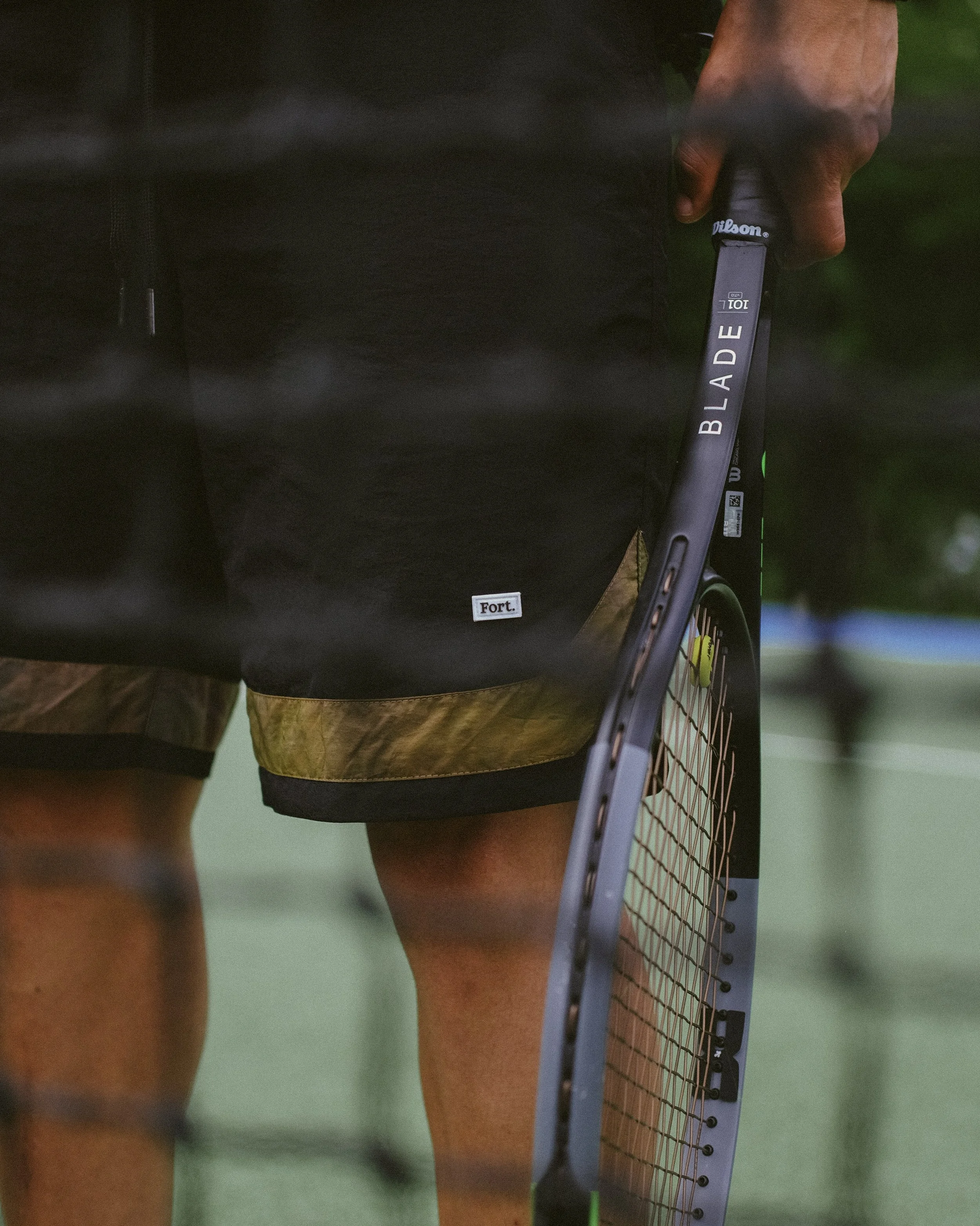Close-up of a person holding a tennis racket with the brand Wilson visible, and wearing athletic clothing, on a tennis court.