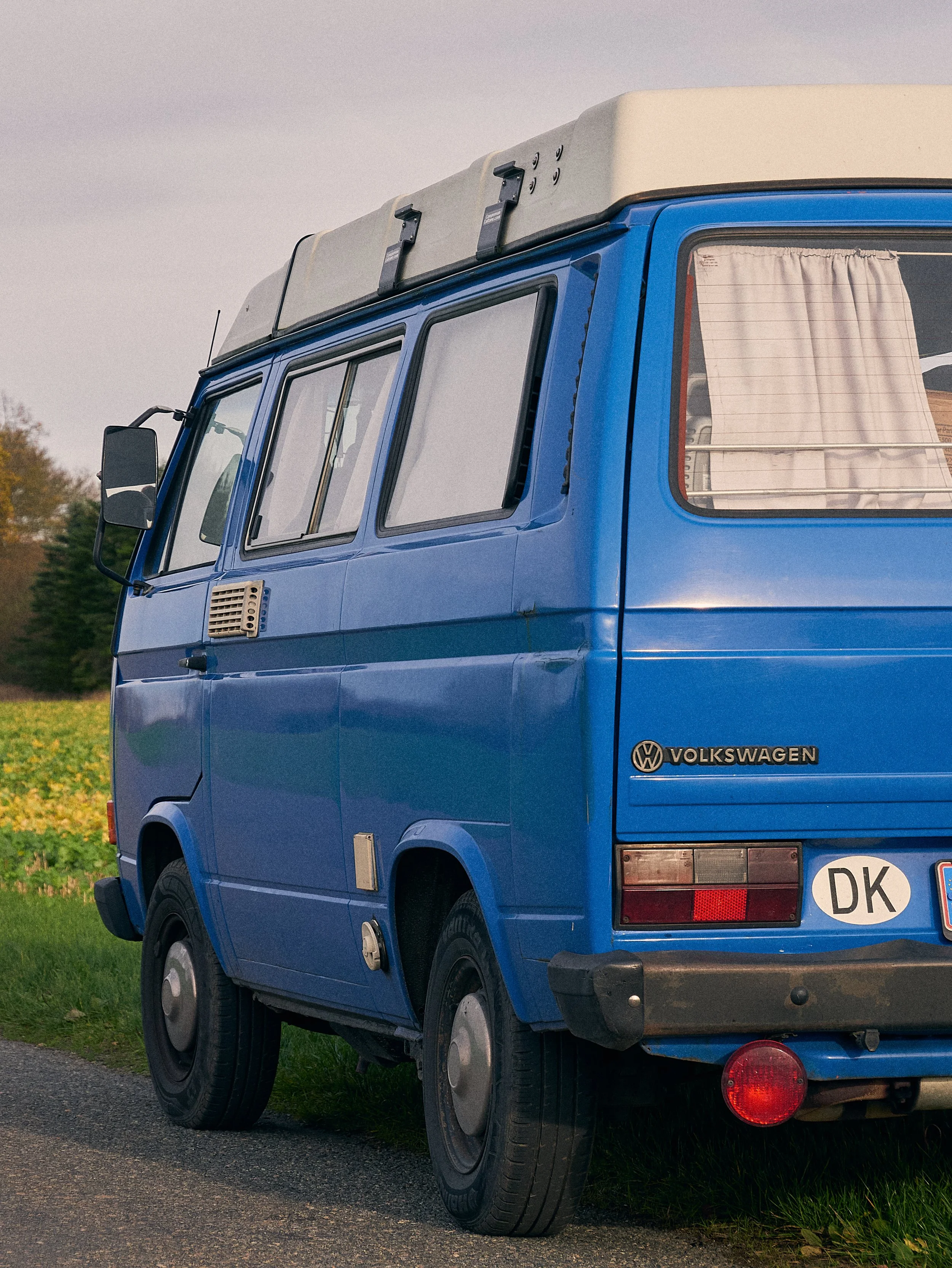 Blue Volkswagen camper van parked on grassy area with a kayak strapped on top.