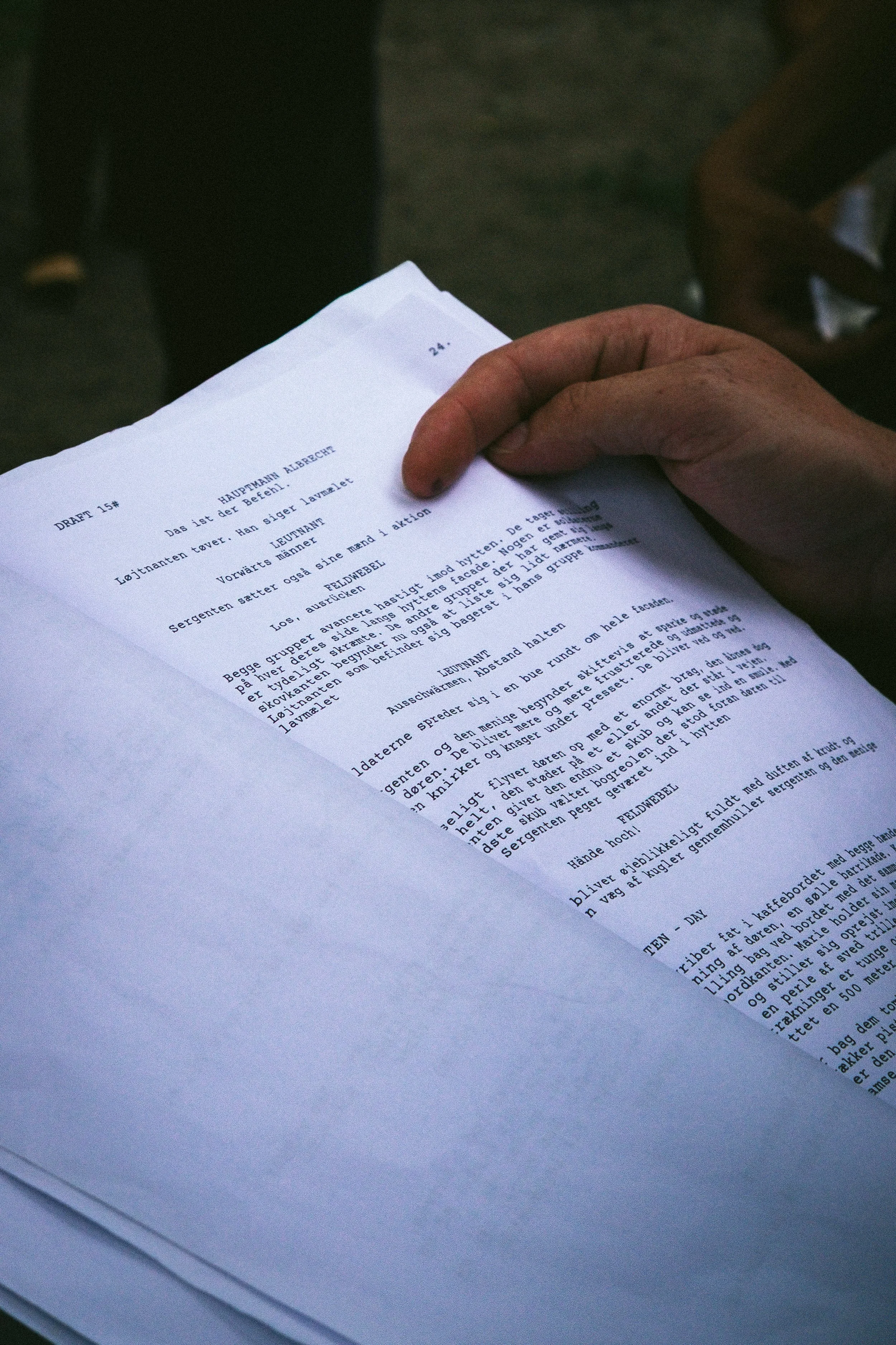 A person holding a printed script or manuscript in their hand, with the text in a foreign language, possibly Scandinavian, on a stack of papers.