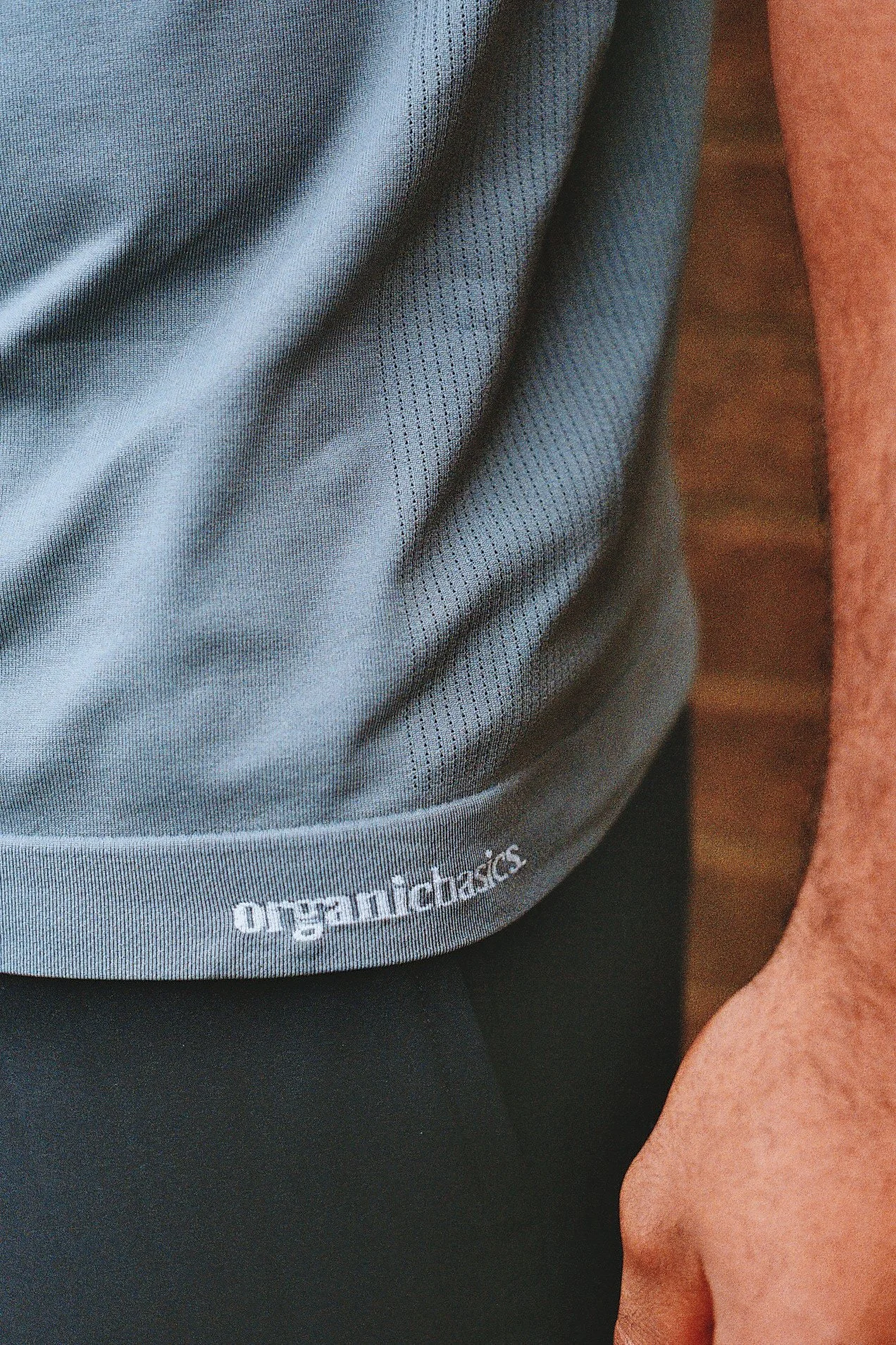 Close-up of a person wearing a gray athletic shirt with the word 'organicdynamics' printed near the bottom, and a tan arm with visible hair resting against a black surface.