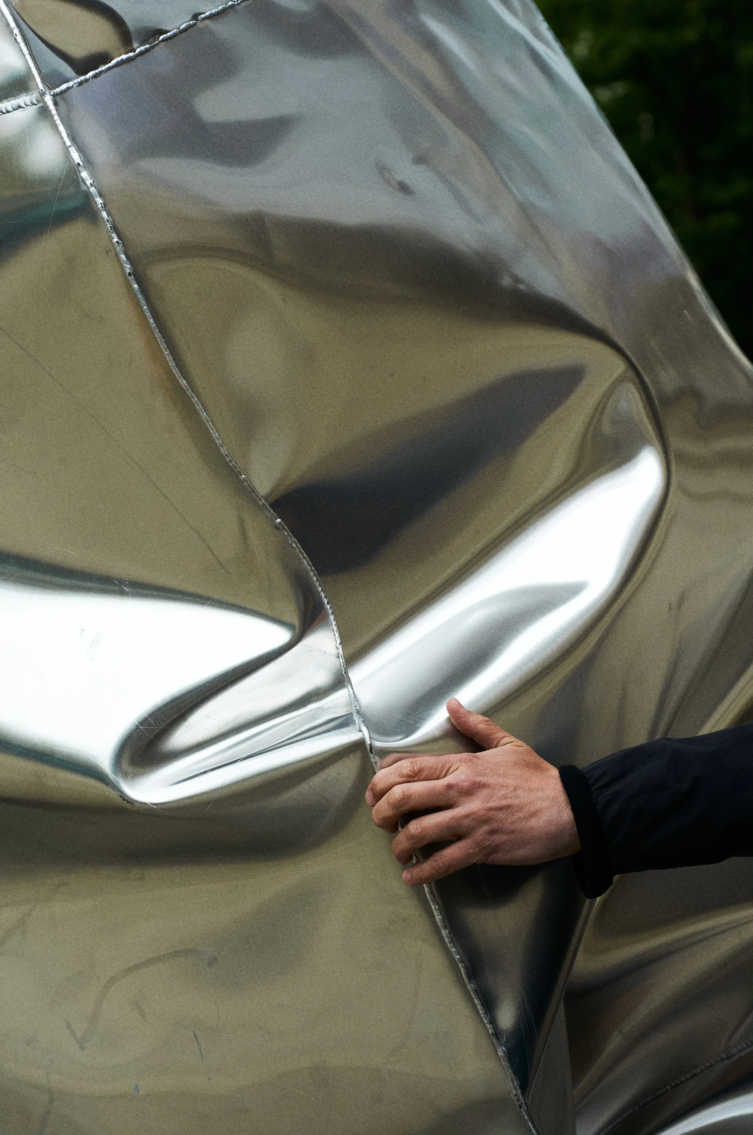 A person with a black long sleeve shirt touching a shiny, warped, reflective metallic surface of a large object.