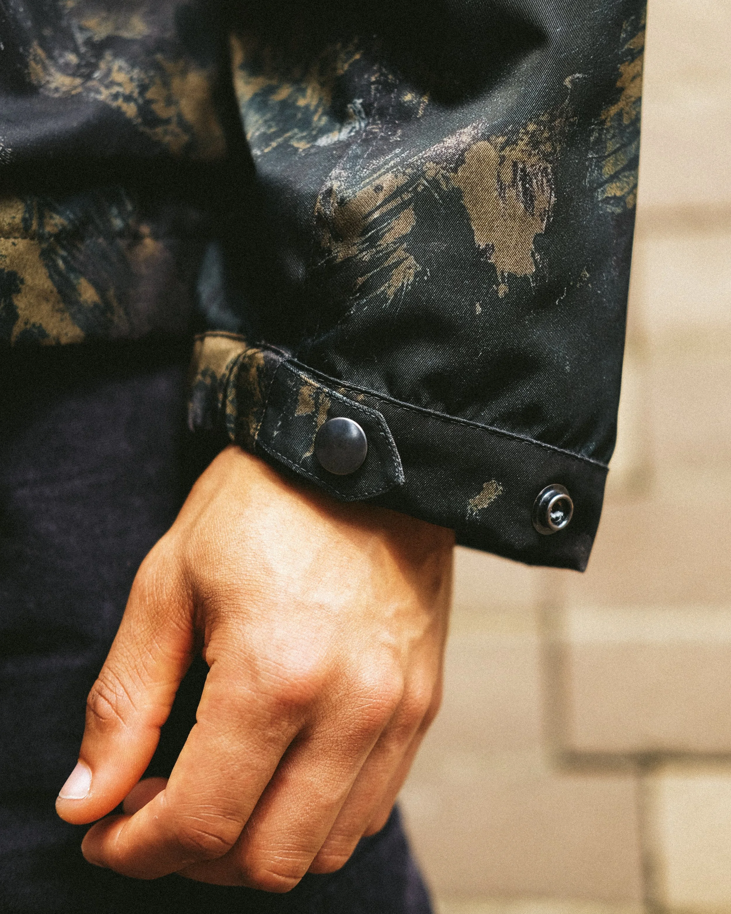 A person's hand holding a black blouse with a gold leaf print and button details.