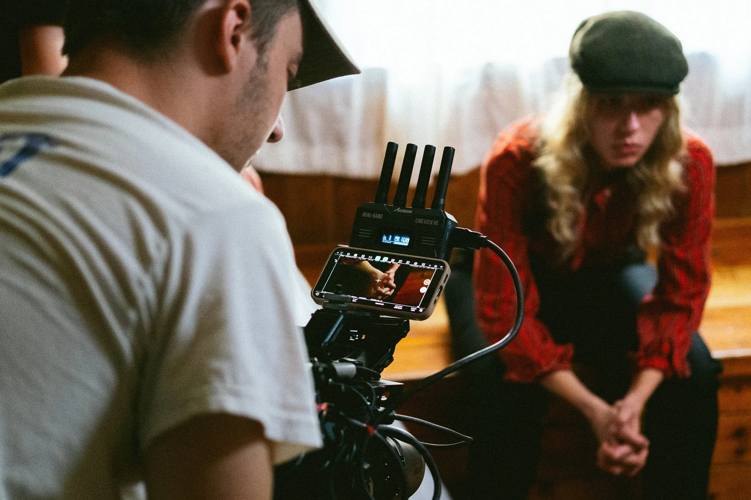 Person operating a professional camera filming a woman in a red outfit with a black hat.