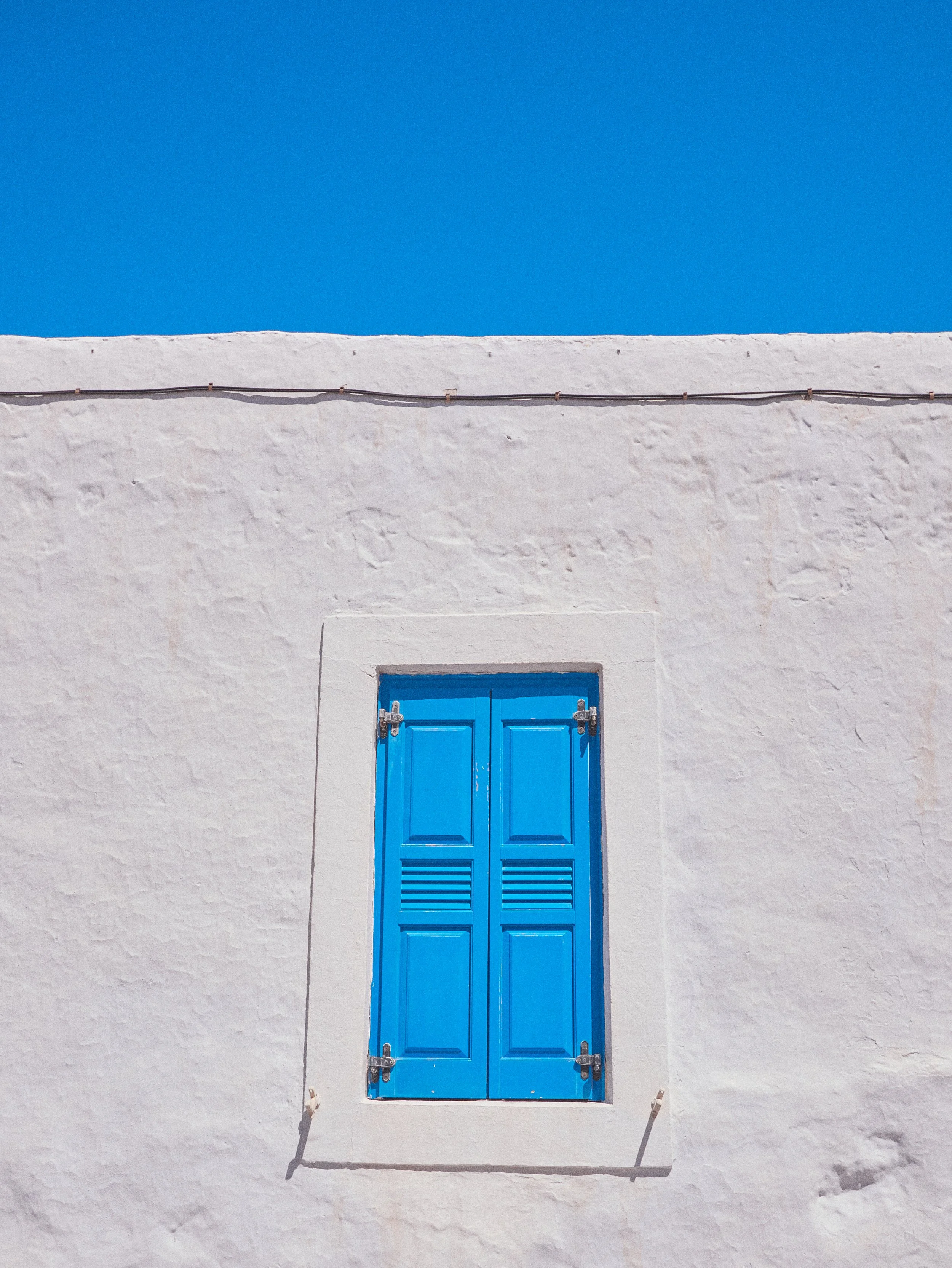 White building with a blue window shutter against a bright blue sky.