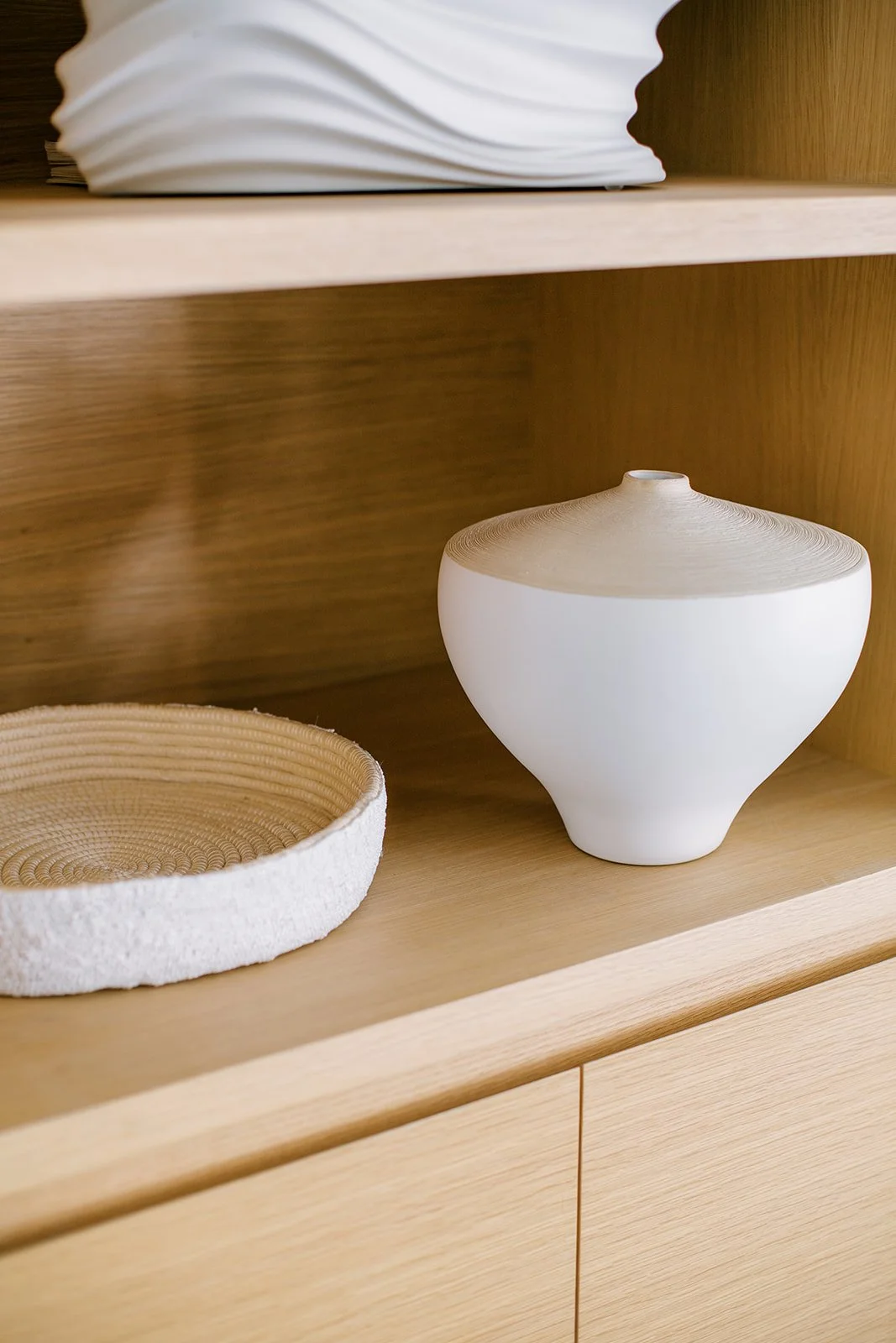 Decorative white ceramic vase with wooden lid on a wooden shelf, next to a woven basket.
