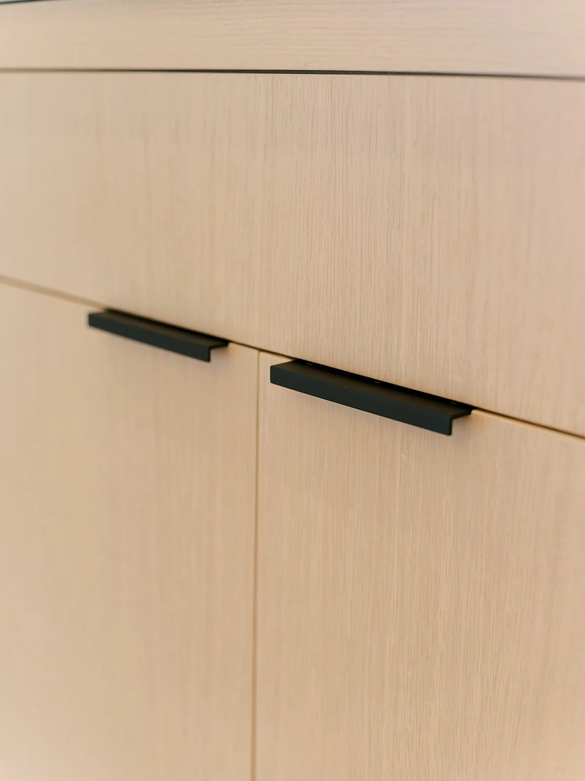 Close-up of light-colored wooden cabinet with black handles.