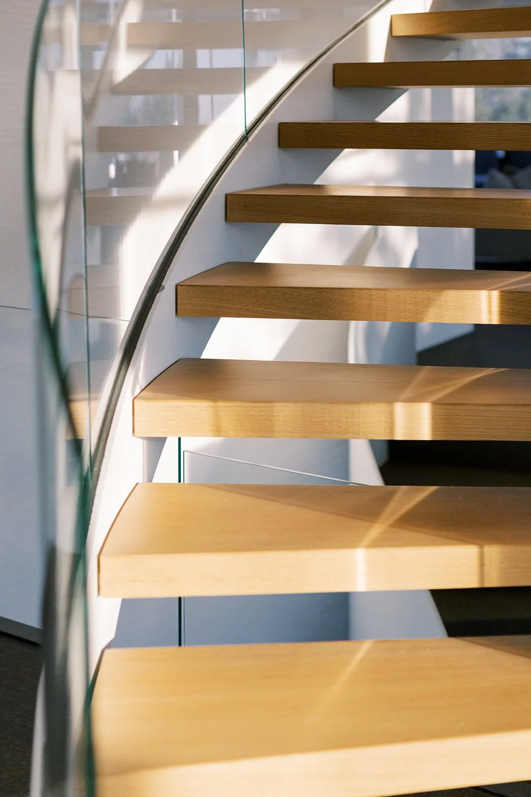 Close-up of a modern wooden staircase with glass railing, sunlight casting shadows on the steps.