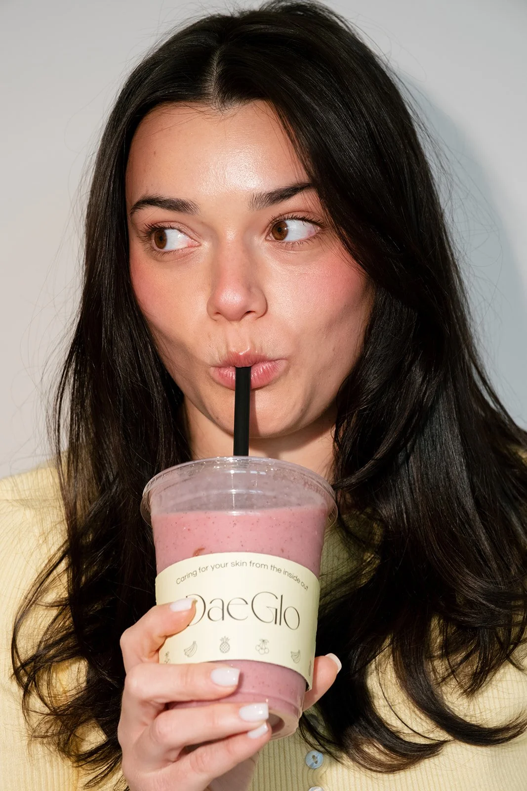 A woman with long dark hair drinking a pink smoothie through a black straw