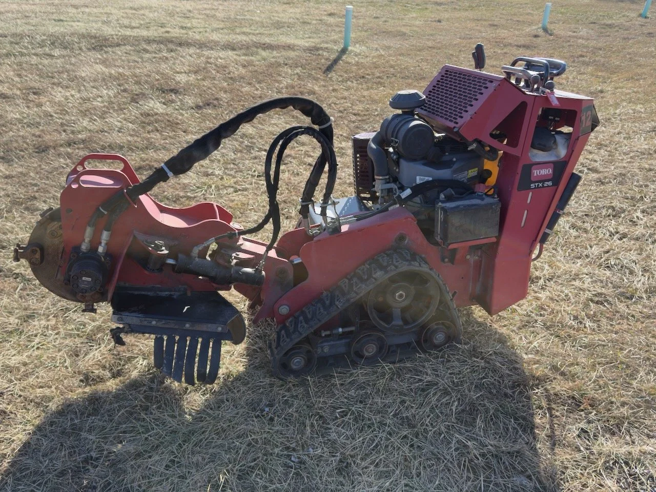 A red trackless snowmobile with a Toro engine, sitting on a dry grassy field with some white poles in the background.