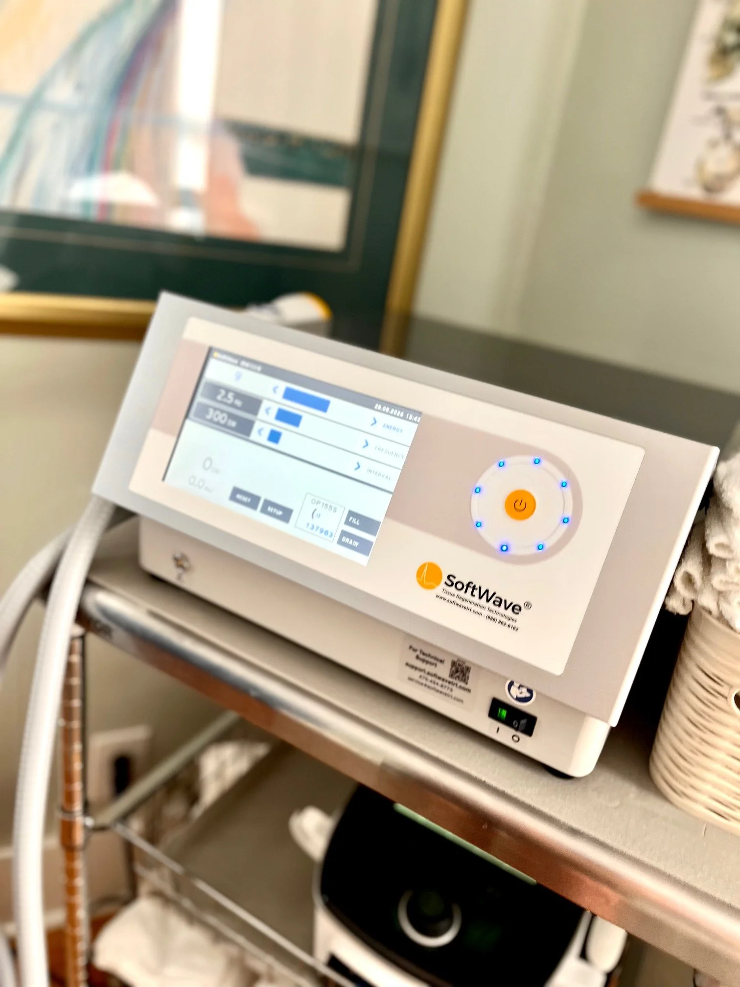 Close-up of a medical device with a digital display showing various readings, placed on a metal cart in a clinical setting.